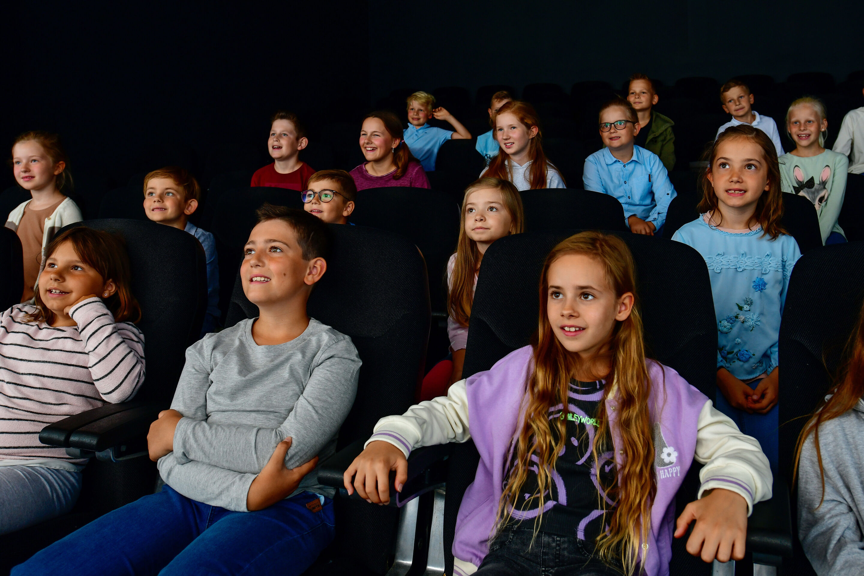 Angebote für Kinder - Einige Mädchen und Jungen sitzen auf Kinosesseln im Audi Programmkino und gucken auf die Leinwand.