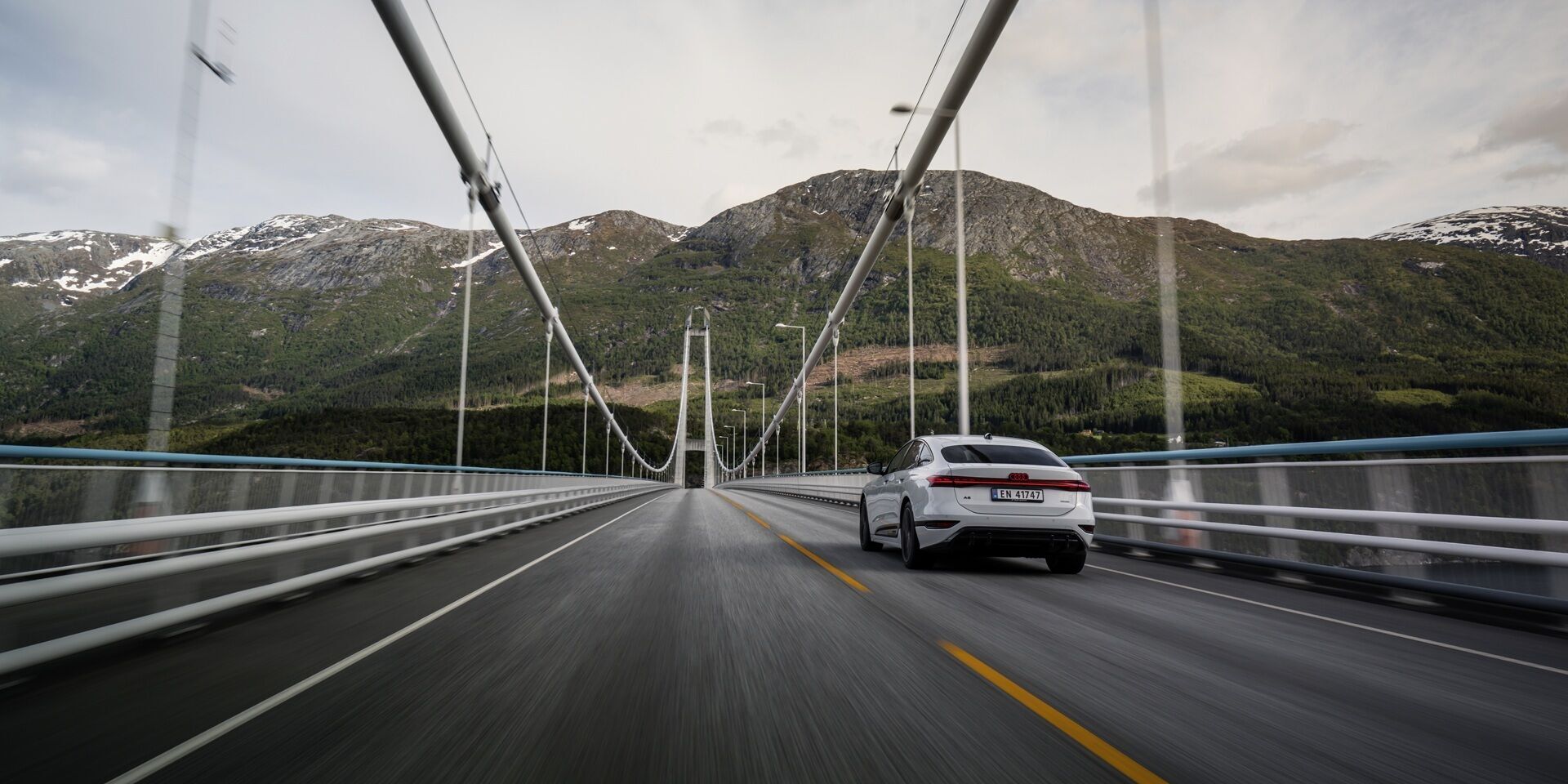 Strom aufwärts: Im Audi A6 e-tron von Kopenhagen nach Bergen - Ein Audi A6 Sportback e-tron in Gletscherweiß Metallic fährt über die Hardangerbrücke in Norwegen. Im Hintergrund befinden sich bewaldete Berge.