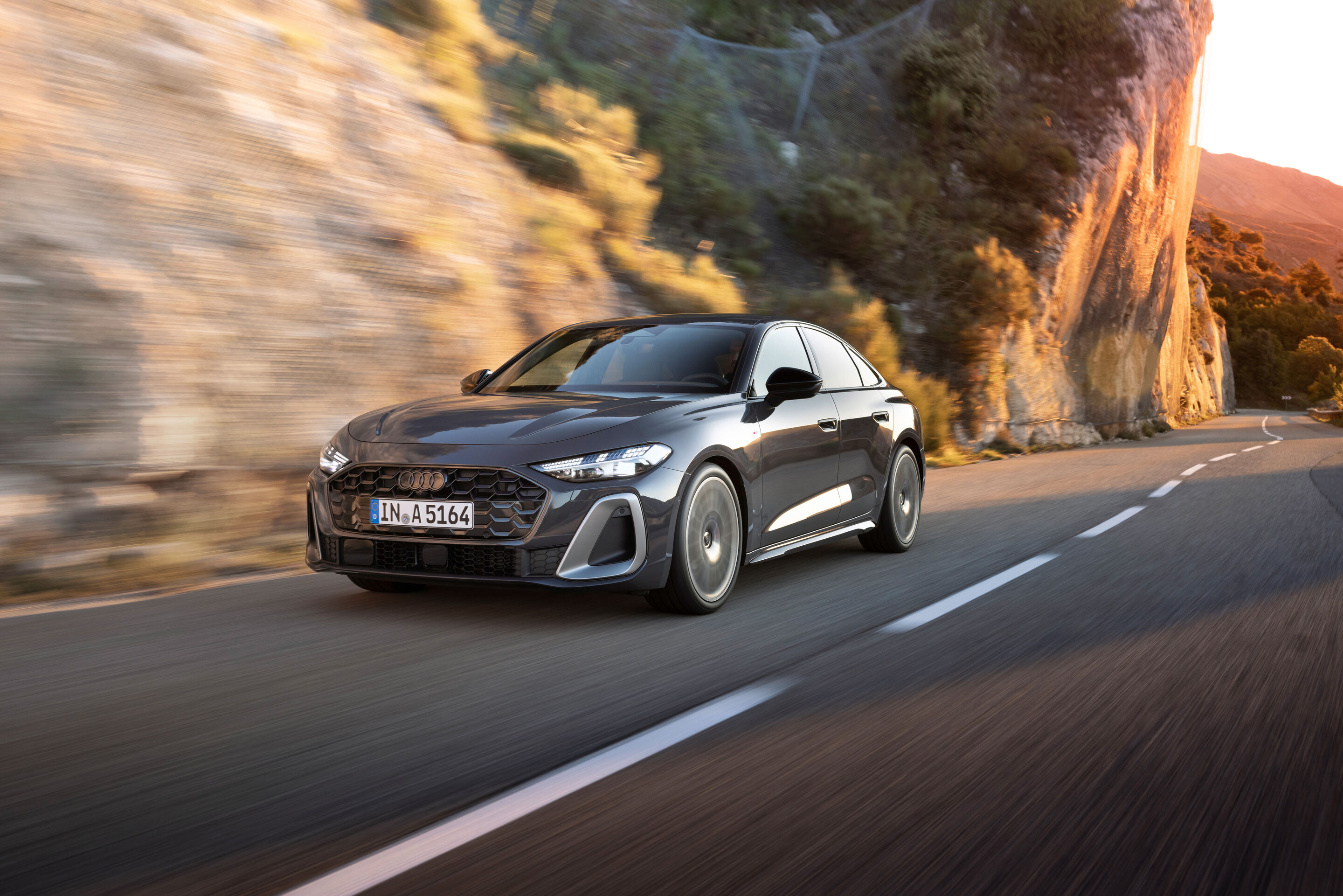 Audi A5 Limousine - Eine Audi A5 Limousine fährt eine Küstenstraße entlang. Im Hintergrund befinden sich steile Felsen. Das Fahrzeug ist in Magnetgrau lackiert.