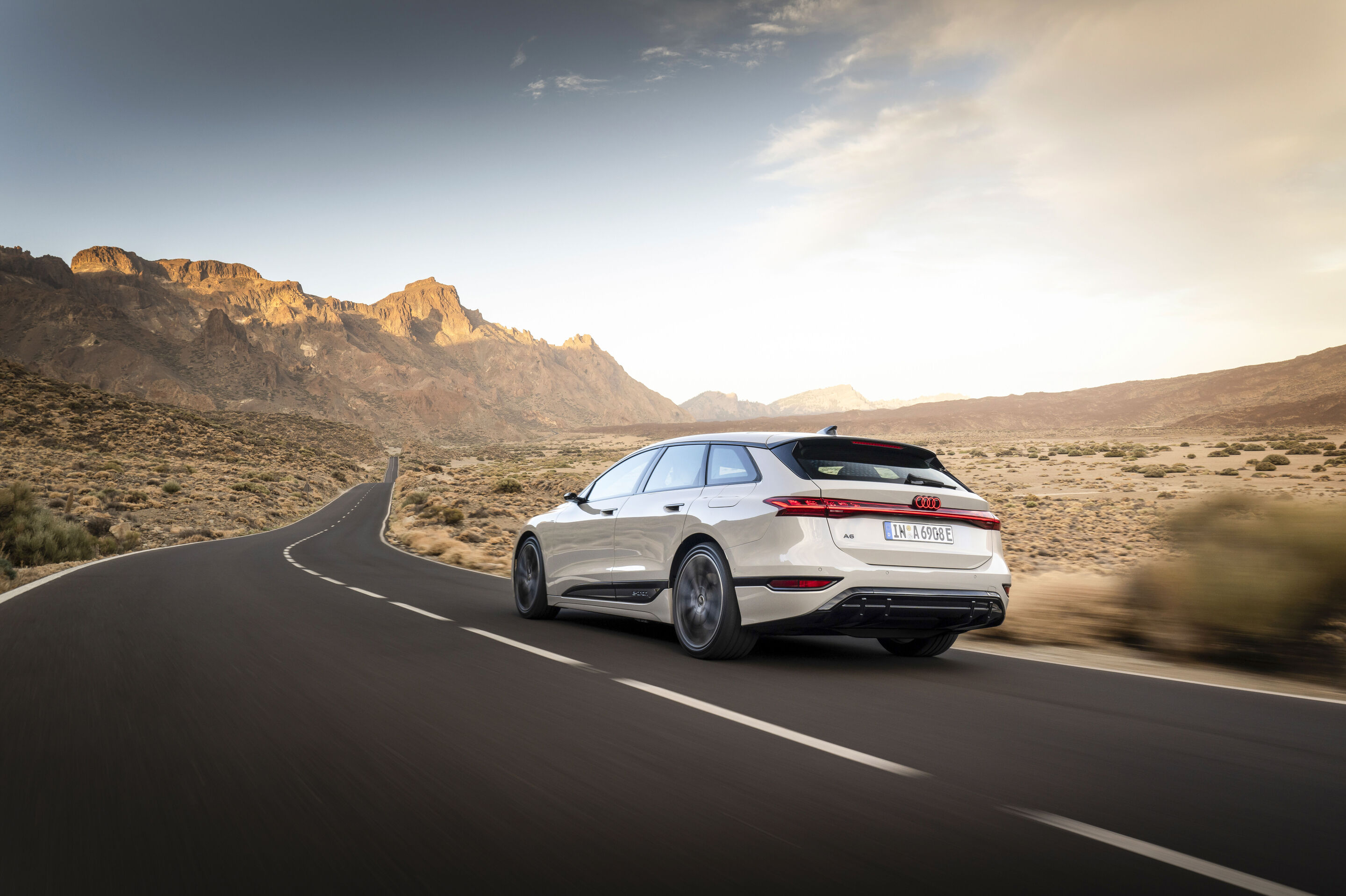 Audi A6 Avant e-tron - Ein Audi A6 Avant e-tron in Siambeige Metallic fährt auf einer Landstraße zwischen einer Dünenlandschaft auf eine Bergkette zu.