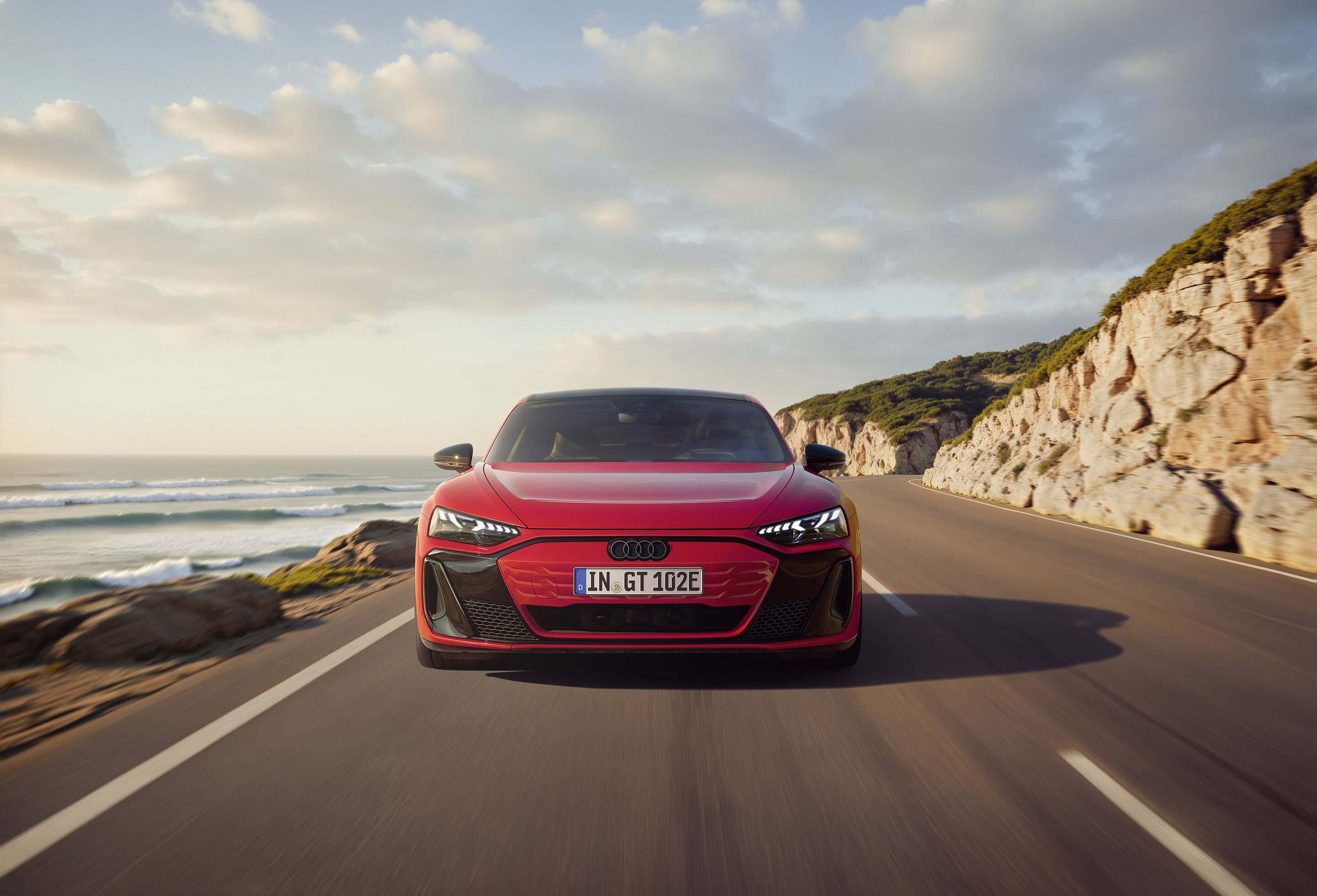 Einstieg in die Spitzenklasse: Audi e-tron GT quattro vereint emotionales Design, Performance und Komfort - An der Front des Audi e-tron GT quattro betont eine schwarze Maske den invertierten Singleframe in Wagenfarbe. Der gezeigte Hintergrund ist KI-generiert.