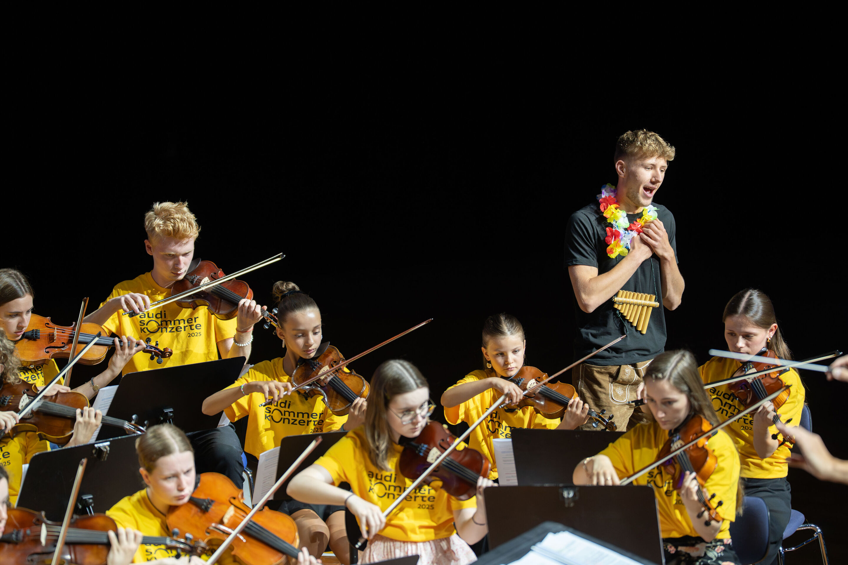 Public workshop with pupils from the region and the Aurora Orchestra - Student Lukas Scheider (12th grade, Wolnzach High School) sings on the right side of the stage in the Ingolstadt festival hall. In front of him, other students can be seen making music.