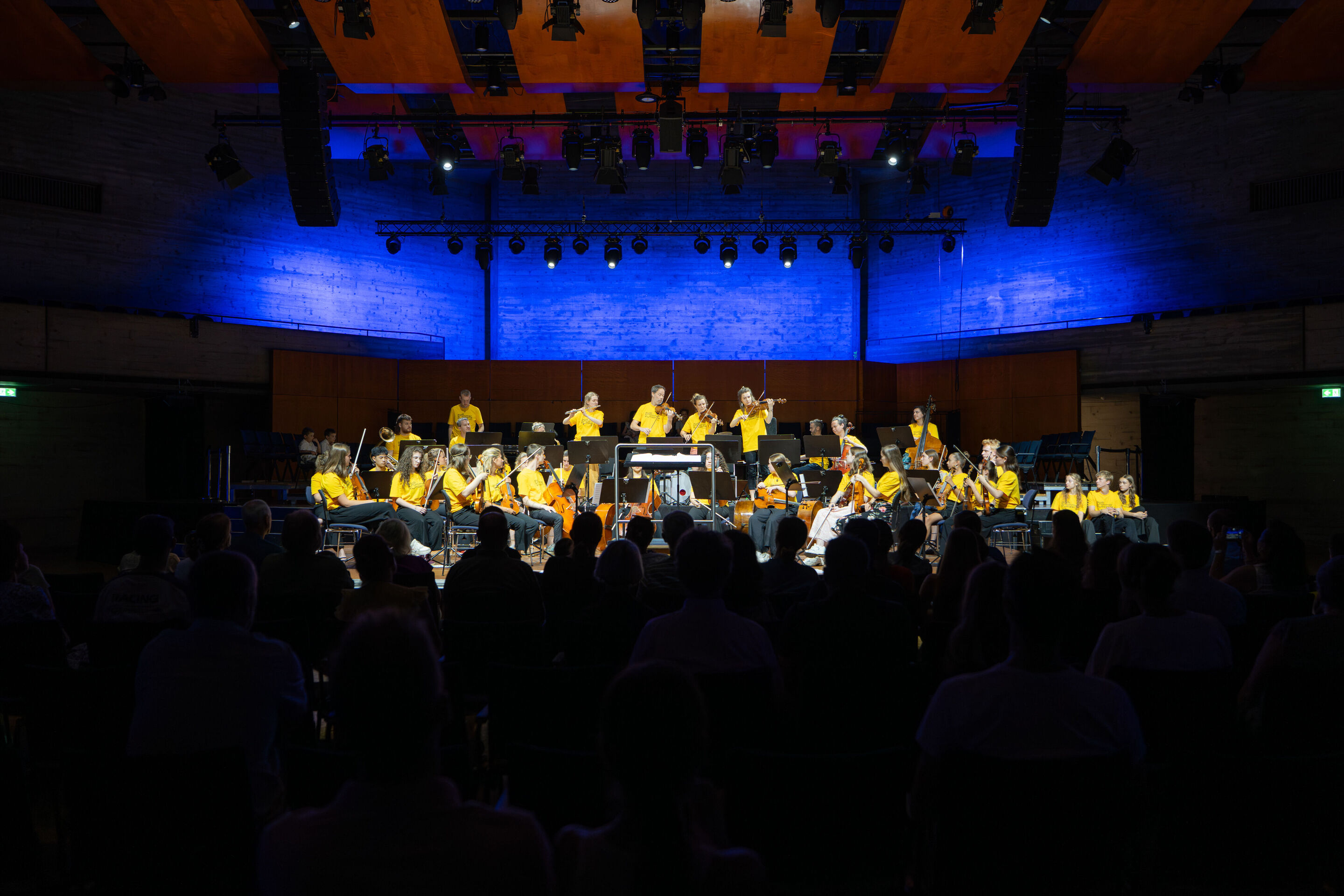 Public workshop with pupils from the region and the Aurora Orchestra - From the audience's perspective, members of the Aurora Orchestra are performing while standing. In front of them, the students are seated with their instruments, watching attentively.