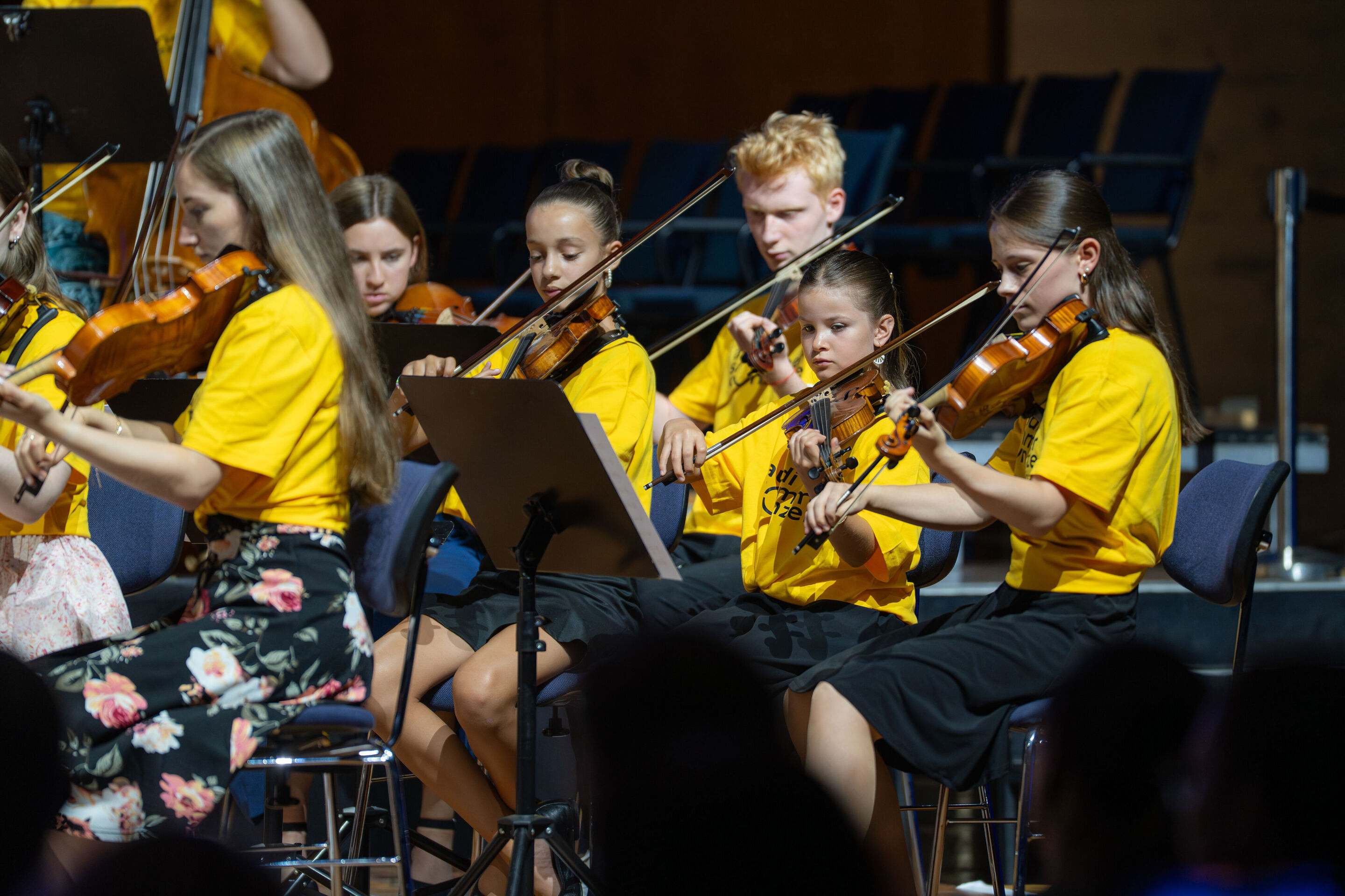 Public workshop with pupils from the region and the Aurora Orchestra - On the stage of the Ingolstadt festival hall, a group of students is performing on their string instruments.