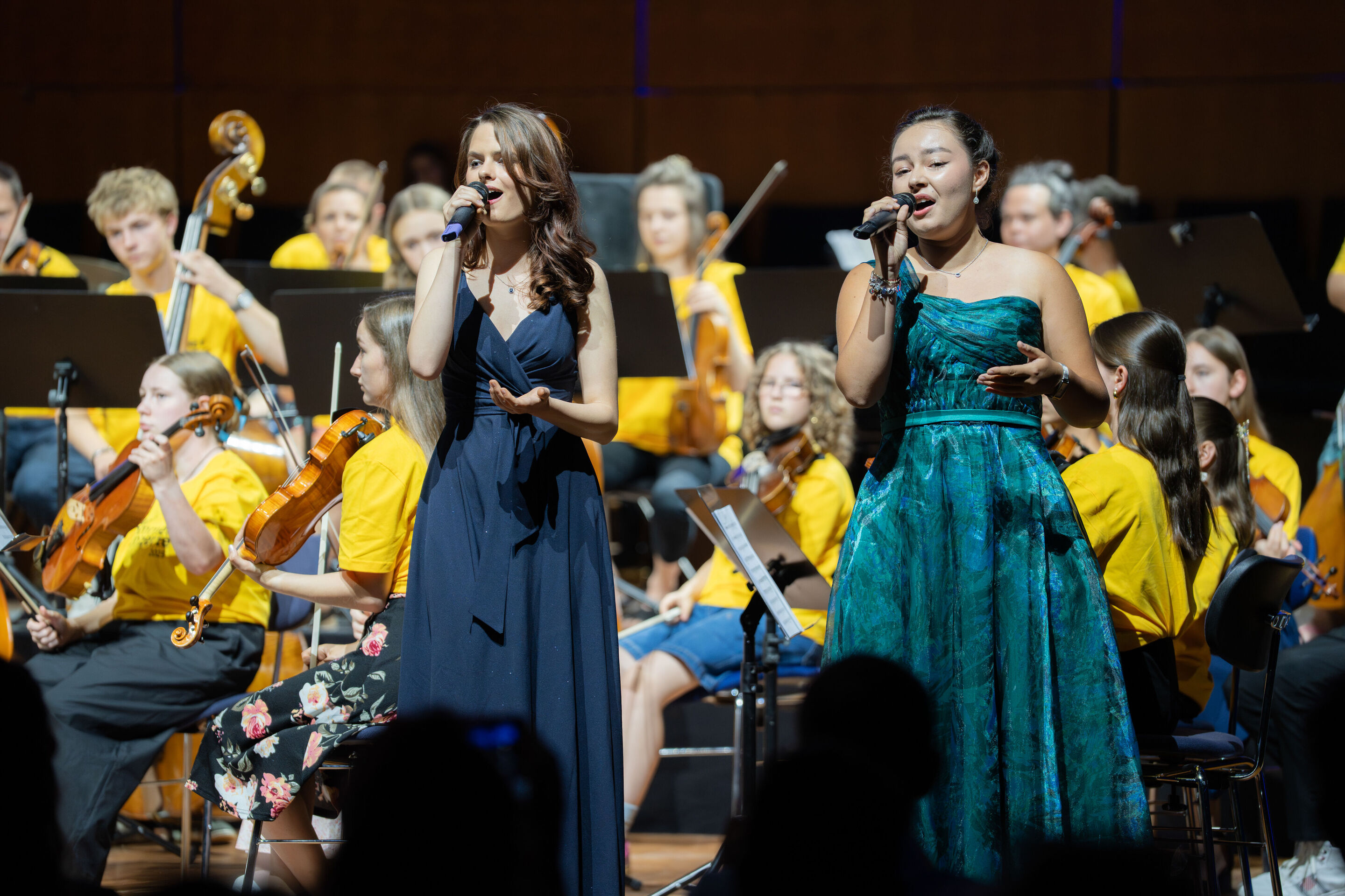 Public workshop with pupils from the region and the Aurora Orchestra - The soloists Sarah Seyfert and Miriam Werner (11th grade students, Gnadenthal-Gymnasium) are singing on the stage of the Ingolstadt festival hall. In the background, seated students...