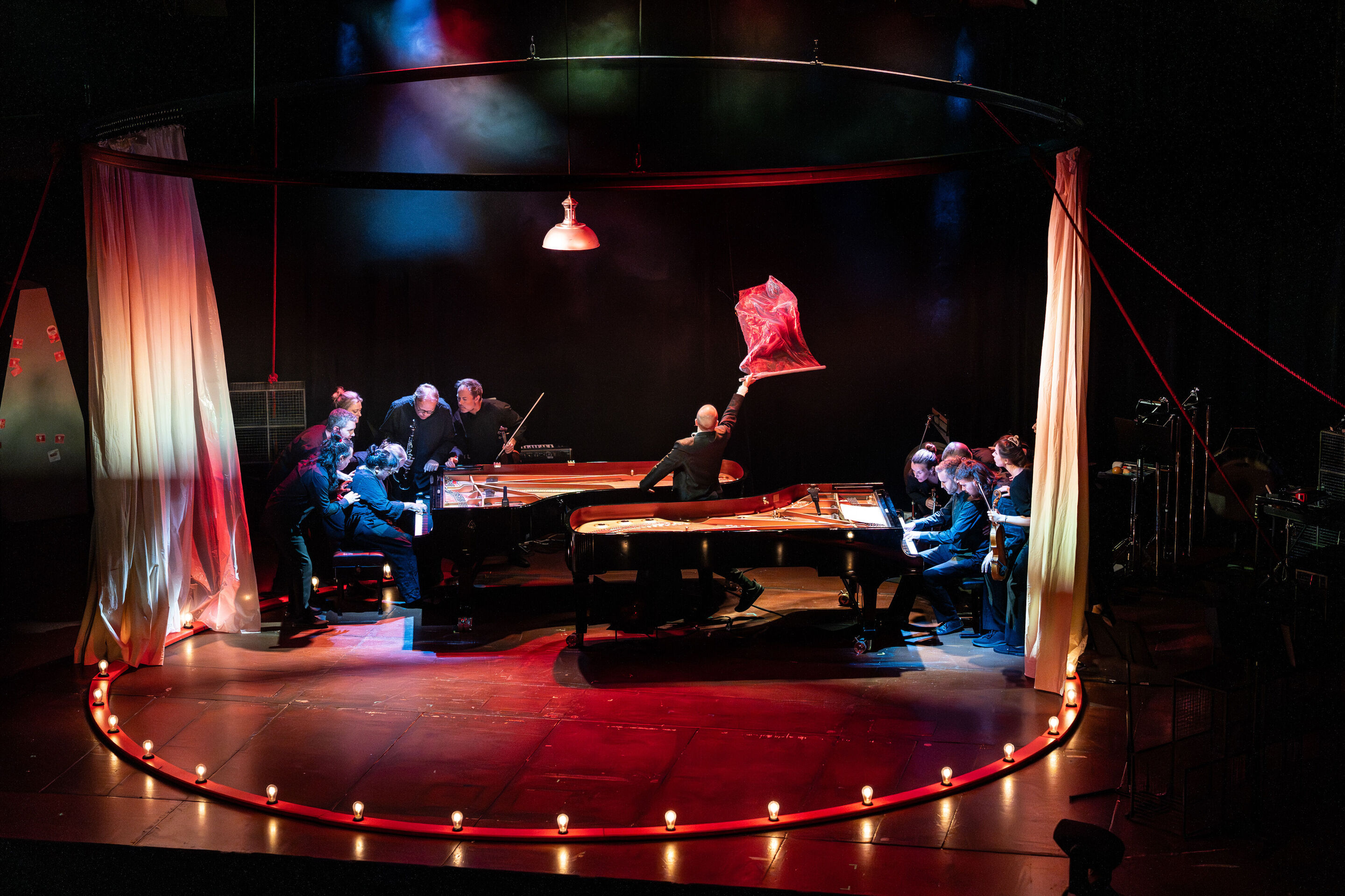 „Carnival“: Inszeniertes Familienkonzert rund um die fabelhafte Welt der Instrumente - Auf der Bühne des Festsaals Ingolstadt sind in einem Lichterkreis zwei Klaviere zu sehen. Um die spielenden Pianisten stehen Mitglieder des Aurora Orchestra. Tänzer...