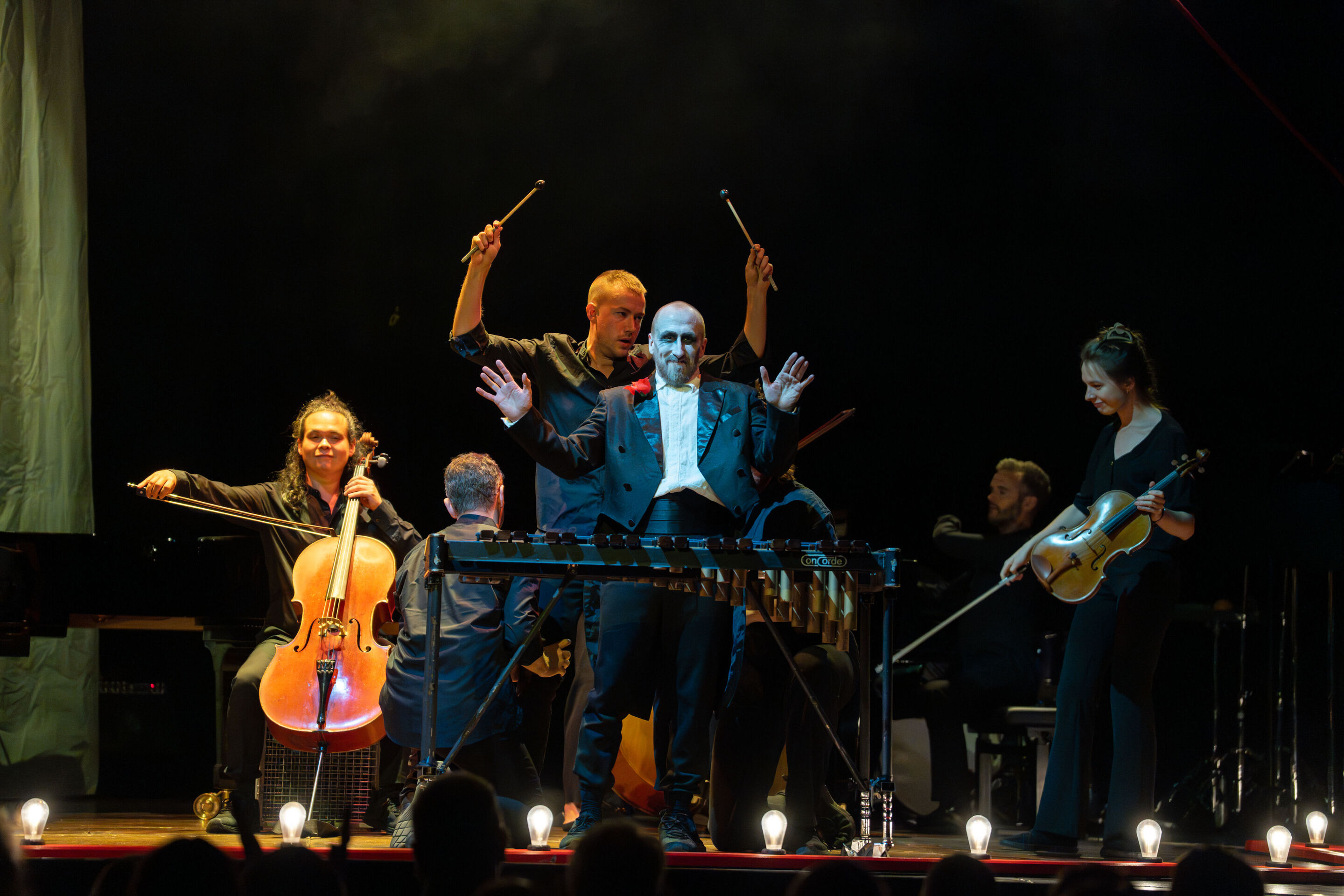 „Carnival“: Inszeniertes Familienkonzert rund um die fabelhafte Welt der Instrumente - Tänzer Christopher Akrill steht vor einem Xylophon mit erhobenen Händen. Hinter ihm sind Mitglieder des Aurora Orchestra mit ihren Instrumenten zu sehen.