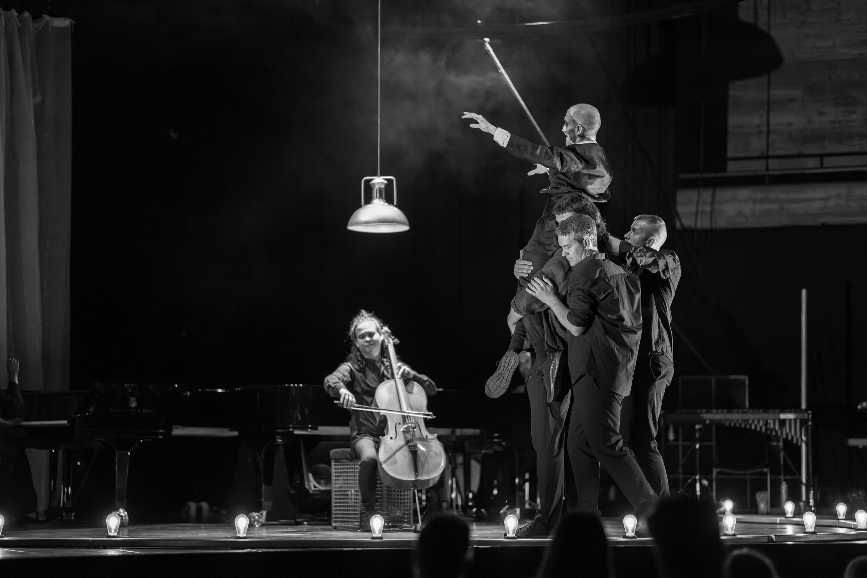 „Carnival“: Inszeniertes Familienkonzert rund um die fabelhafte Welt der Instrumente - Auf der Bühne des Festsaals Ingolstadt spielt ein Mitglied des Aurora Orchestra auf seinem Cello. Davor heben einige männliche Mitglieder des Aurora Orchestra Tänzer...