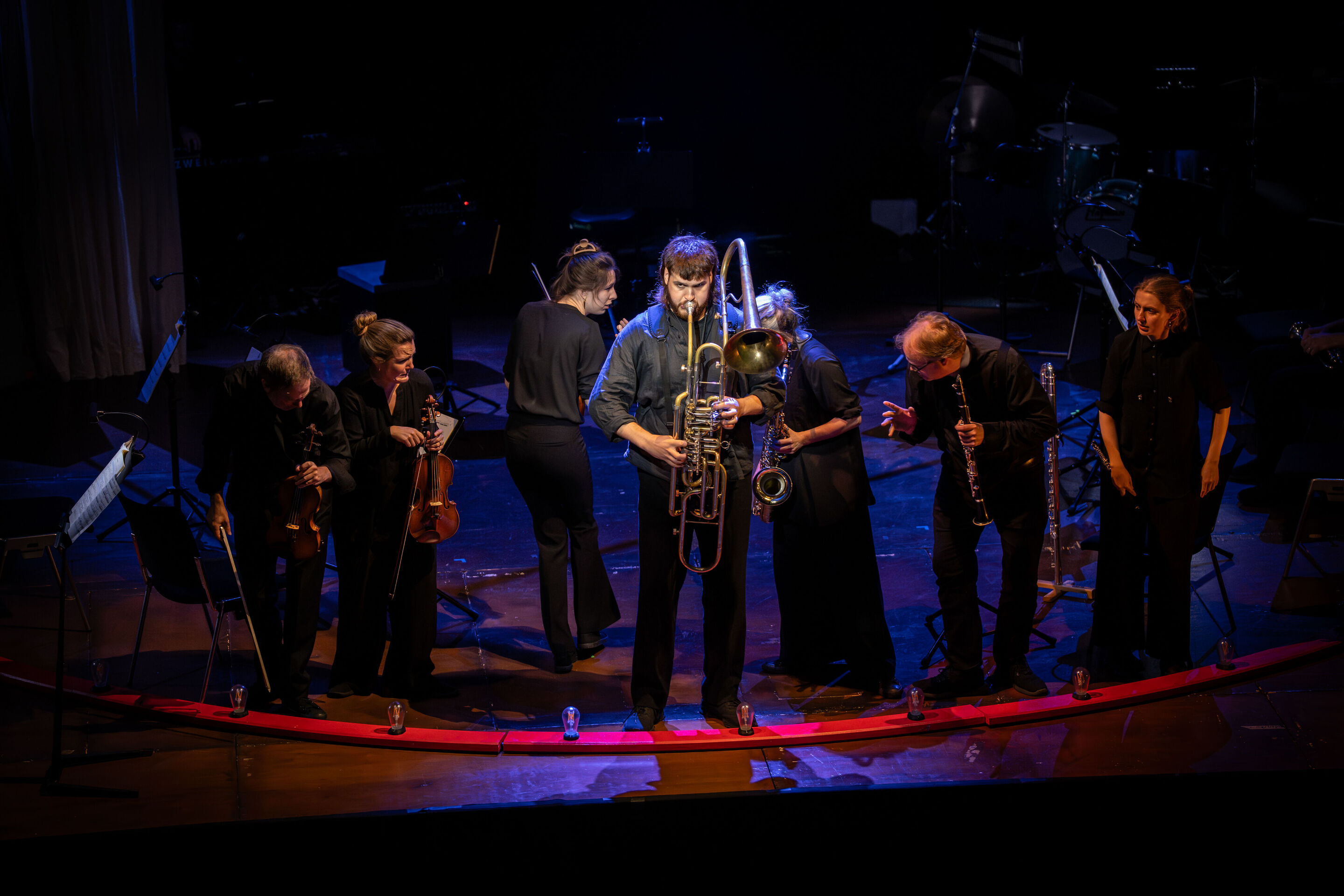 „Carnival“: Inszeniertes Familienkonzert rund um die fabelhafte Welt der Instrumente - Auf der Bühne des Festsaals Ingolstadt spielt ein Mitglied des Aurora Orchestra auf einem Cimbasso. Hinter ihm sind weitere Mitglieder des Orchesters zu sehen.