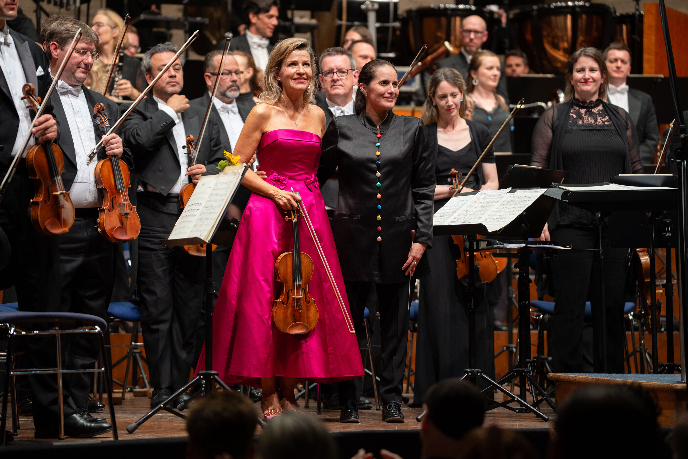 „Across the Stars“: Filmmusik mit Weltstar Anne-Sophie Mutter und dem Royal Philharmonic Orchestra - Star-Geigerin Anne-Sophie Mutter steht Arm in Arm mit Dirigentin Lina González-Granados auf der Bühne des Festsaal Ingolstadt. Dahinter sind Musizierende...