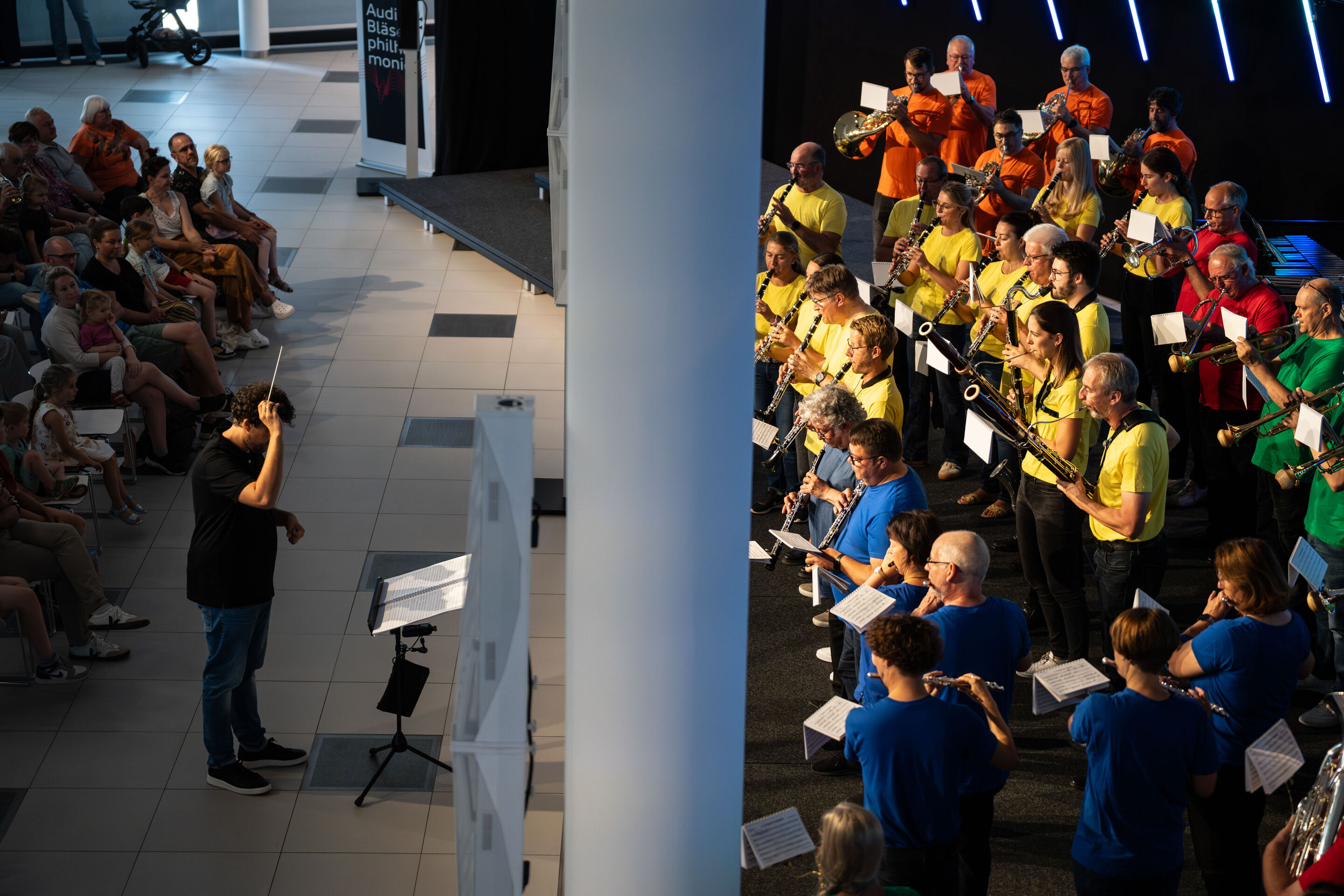 „ADUI und die Kraft der magischen Ringe“: Kinderkonzert mit der Audi Bläserphilharmonie - Beim Kinderkonzert ADUI im H6 am Standort Ingolstadt leitet Dirigent Pietro Sarno die Audi Bläserphilharmonie. Links im Bild verfolgt das Publikum aufmerksam das...