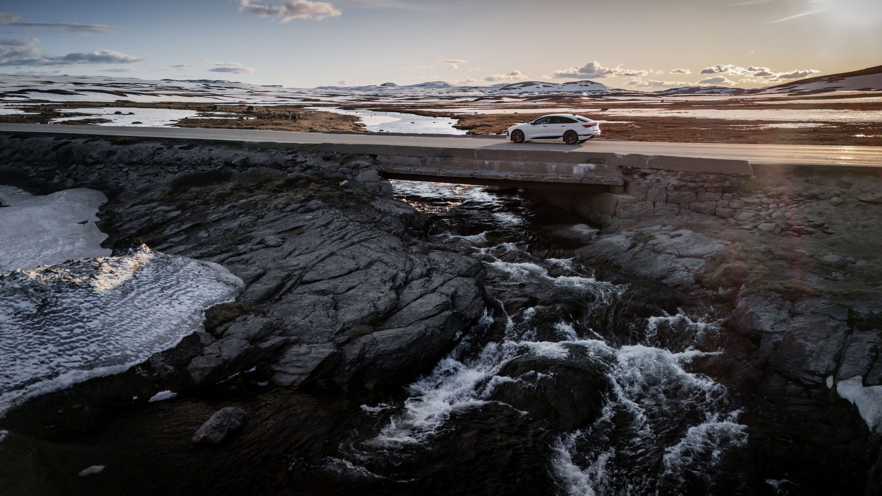 Strom aufwärts: Im Audi A6 e-tron von Kopenhagen nach Bergen - Ein Audi A6 Sportback e-tron in Gletscherweiß Metallic überquert eine kurze Brücke, unter der ein wilder Fluss entlangläuft. Im Hintergrund liegt die weite Landschaft Norwegens.