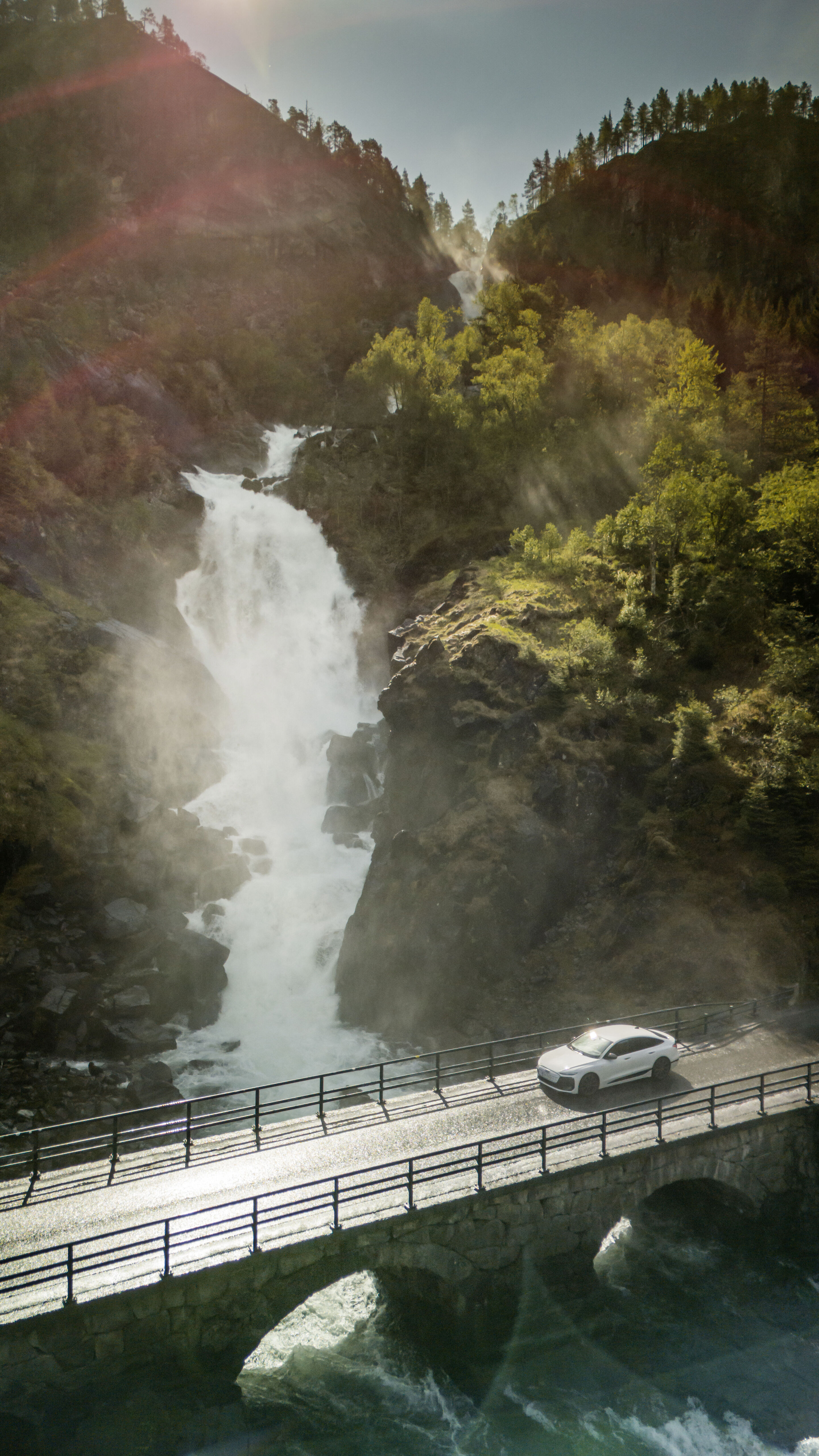 Strom aufwärts: Im Audi A6 e-tron von Kopenhagen nach Bergen - Ein Audi A6 Sportback e-tron in Gletscherweiß Metallic überquert eine Brücke, im Hintergrund befindet sich ein spektakulärer Wasserfall.