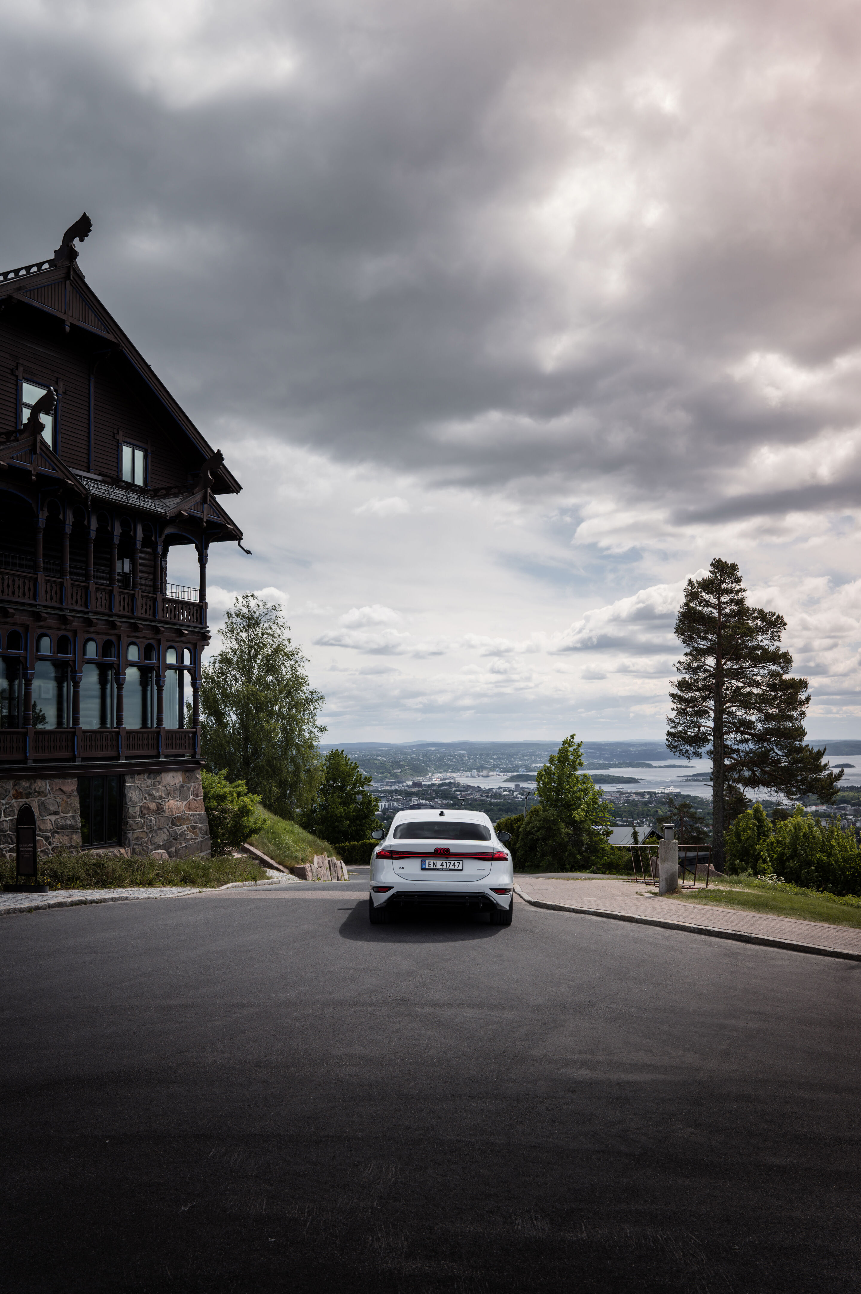 Strom aufwärts: Im Audi A6 e-tron von Kopenhagen nach Bergen - Ein Audi A6 Sportback e-tron in Gletscherweiß Metallic steht rechts von einem Hotel skandinavischer Bauweise, in der Ferne ist Oslo zu sehen.