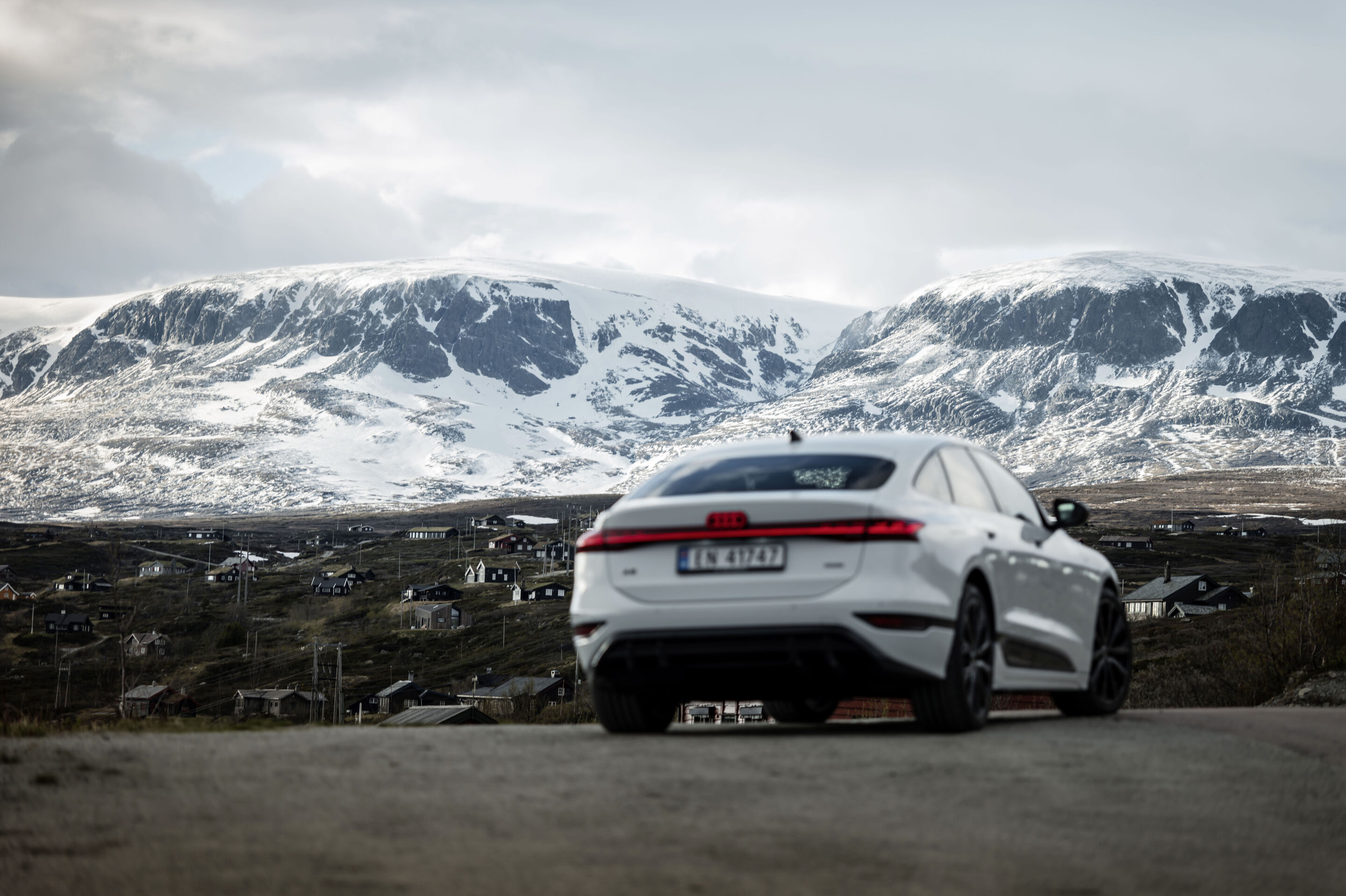 Strom aufwärts: Im Audi A6 e-tron von Kopenhagen nach Bergen - Ein Audi A6 Sportback e-tron in Gletscherweiß Metallic steht auf einer Straße, dahinter befindet sich ein norwegisches Dorf mit zahlreichen verstreuten Häusern sowie stark verschneiten Bergen.