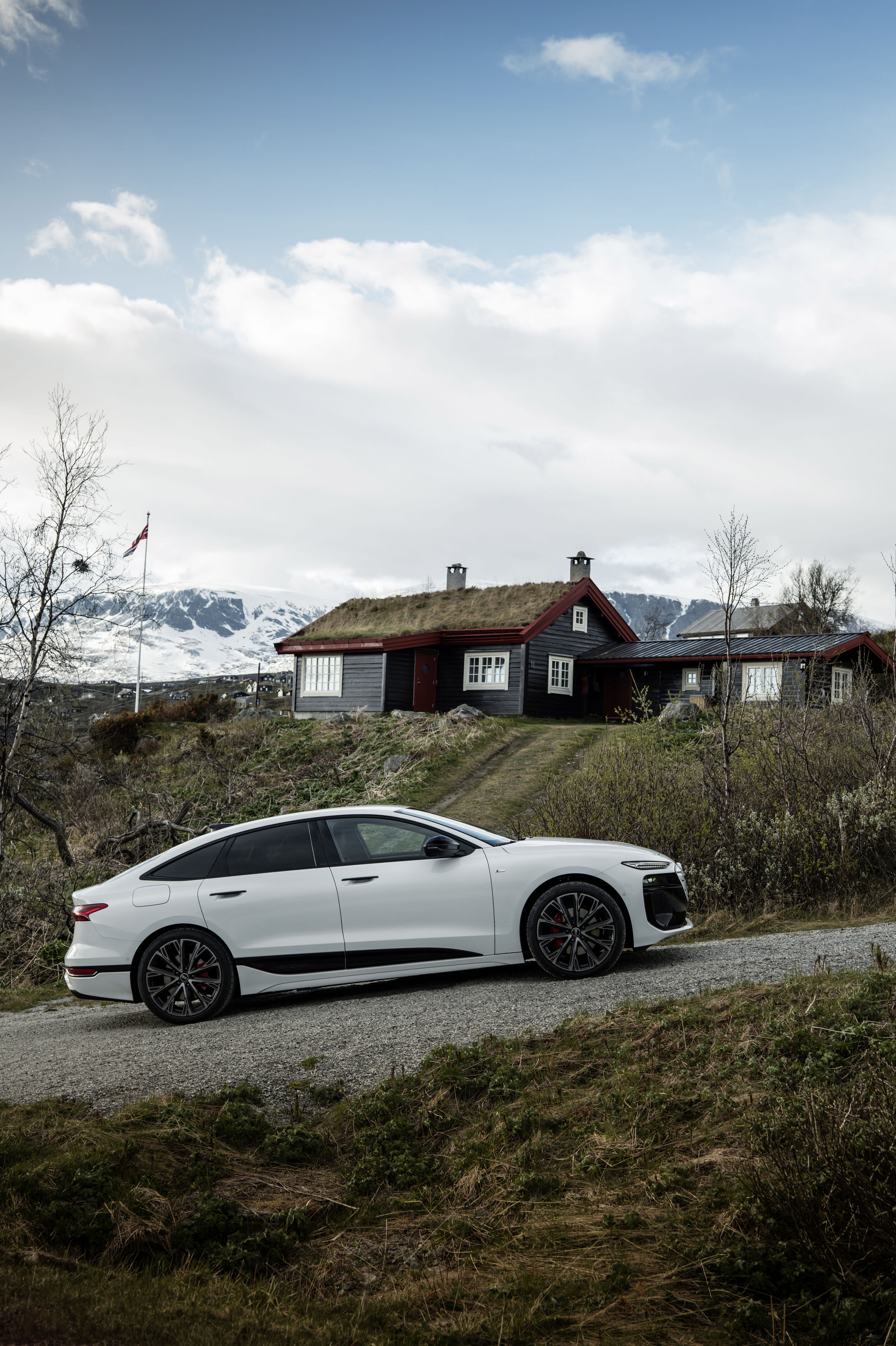 Strom aufwärts: Im Audi A6 e-tron von Kopenhagen nach Bergen - Ein Audi A6 Sportback e-tron in Gletscherweiß Metallic steht unweit eines Hauses, das klassischer norwegischer Bauweise entspricht.