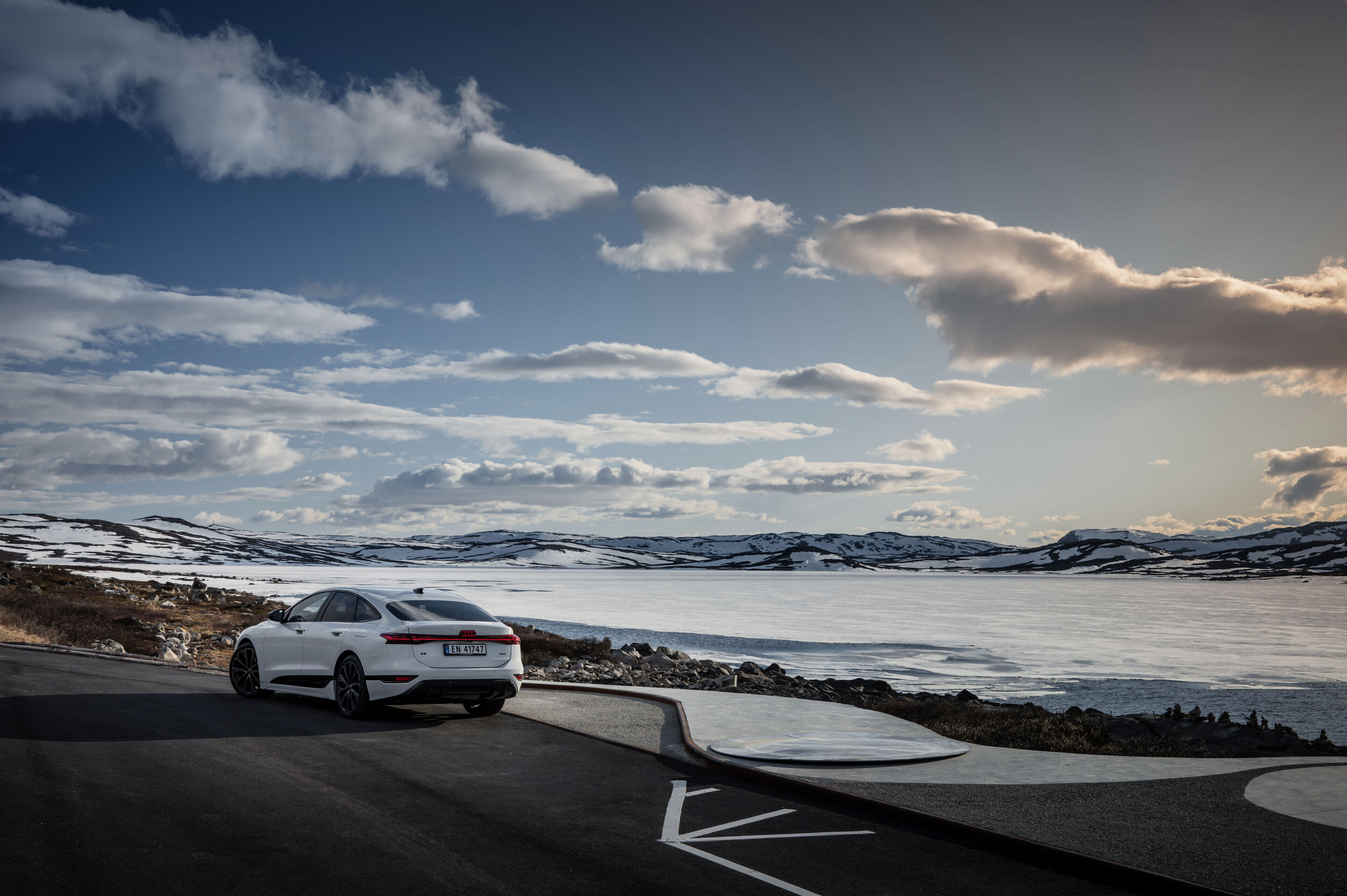 Strom aufwärts: Im Audi A6 e-tron von Kopenhagen nach Bergen - Ein Audi A6 Sportback e-tron in Gletscherweiß Metallic steht auf einem Parkplatz in Norwegen. Im Hintergrund befindet sich vereistes Gewässer mit verschneiten Hügeln.