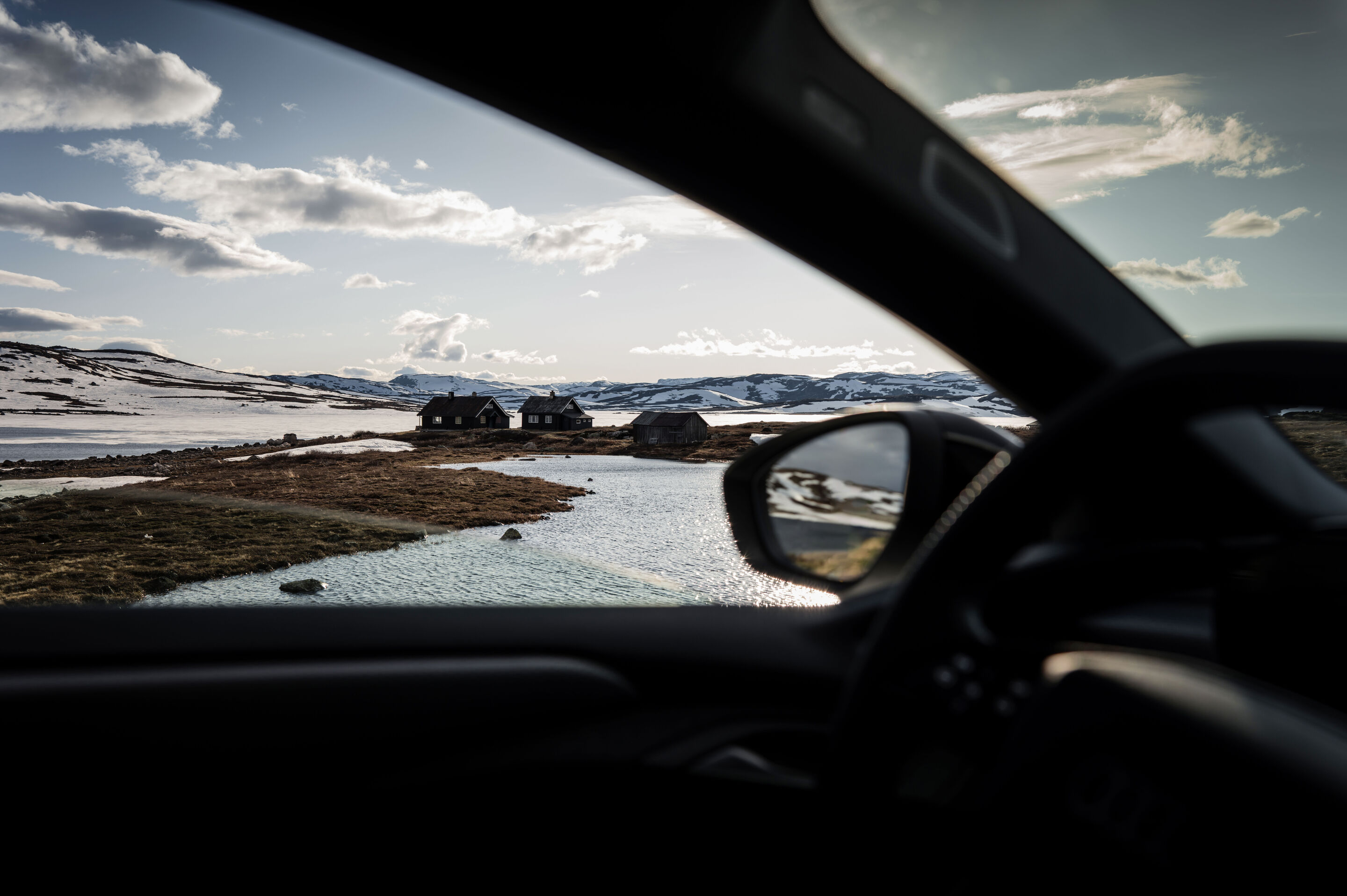 Strom aufwärts: Im Audi A6 e-tron von Kopenhagen nach Bergen - Aus dem Innenraum eines Audi A6 Sportback e-tron fällt der Blick auf eine Ansammlung von drei Häusern norwegischer Bauart mit Wasser im Vordergrund. Im Hintergrund befindet sich die verschneite...