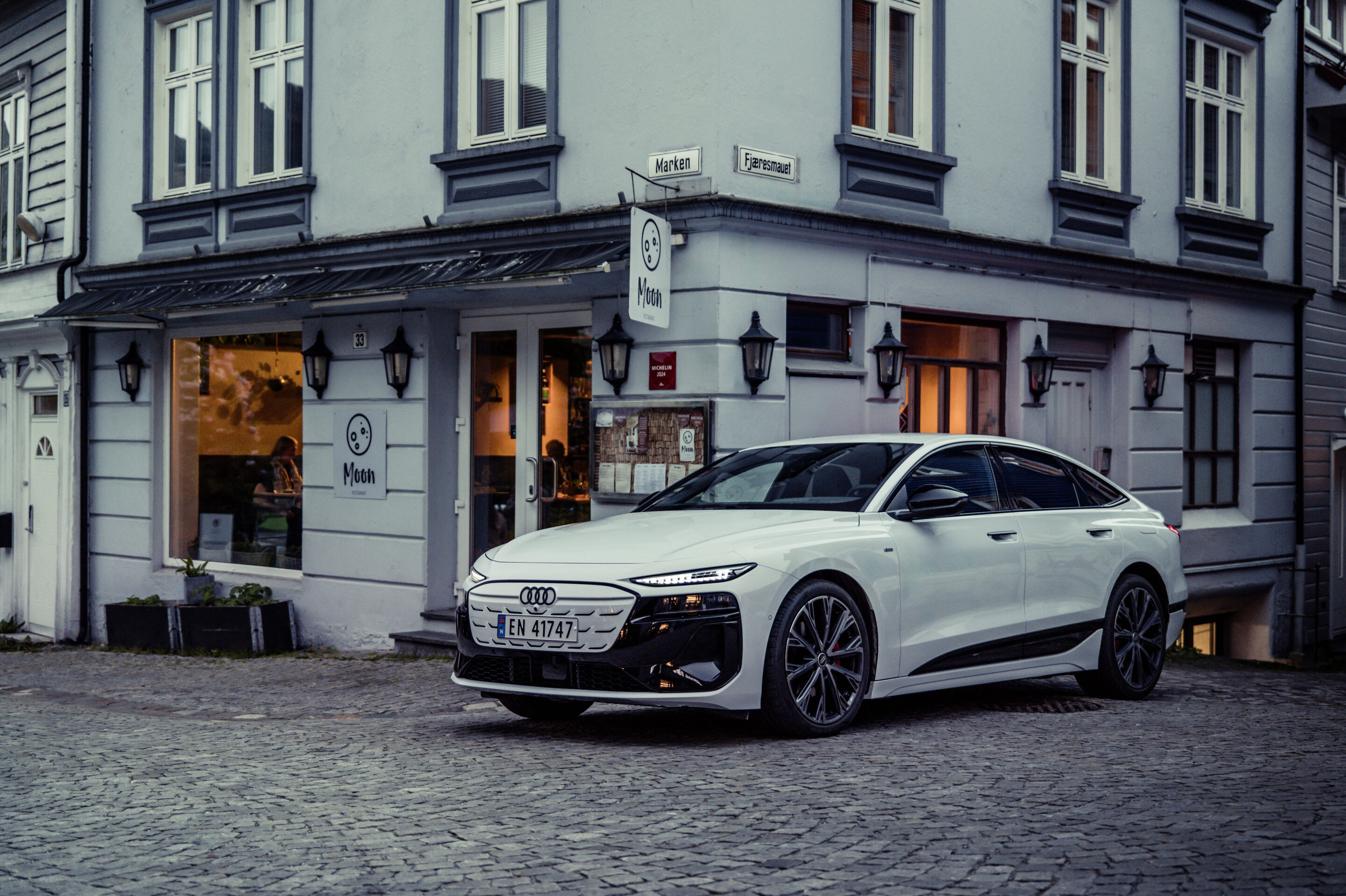 Strom aufwärts: Im Audi A6 e-tron von Kopenhagen nach Bergen - Ein Audi A6 Sportback e-tron in Gletscherweiß Metallic steht vor einem Restaurant in der norwegischen Stadt Bergen.