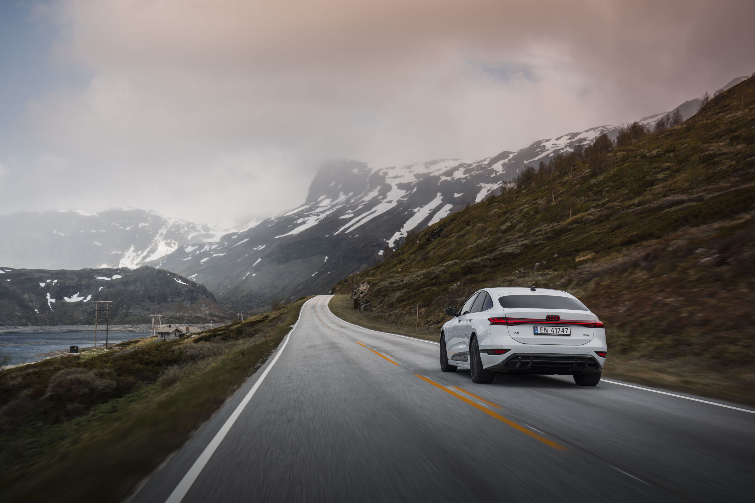 Strom aufwärts: Im Audi A6 e-tron von Kopenhagen nach Bergen - Ein Audi A6 Sportback e-tron in Gletscherweiß Metallic fährt eine Straße in der norwegischen Landschaft entlang. Im Hintergrund befinden sich verschneite Berge.