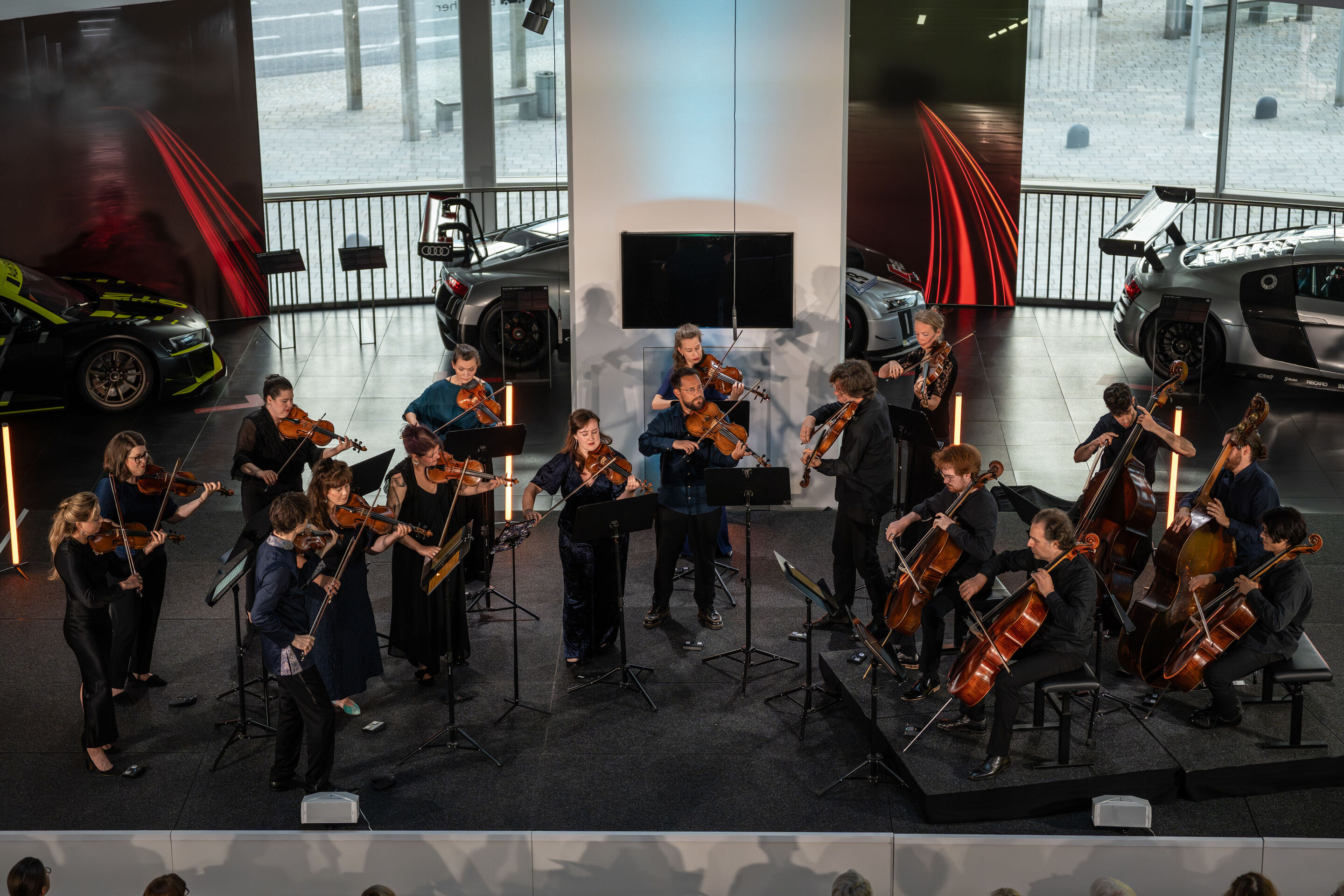 „Crossing over the Atlantic“: von Britten bis Nirvana mit dem O/Modernt Kammerorchester - Von oben: Auf der Bühne des Audi museum mobile steht das O Modernt Kammerorchester unter der Leitung von Hugo Ticciati. Dahinter Ausstellungsstücke der „Audi R8...