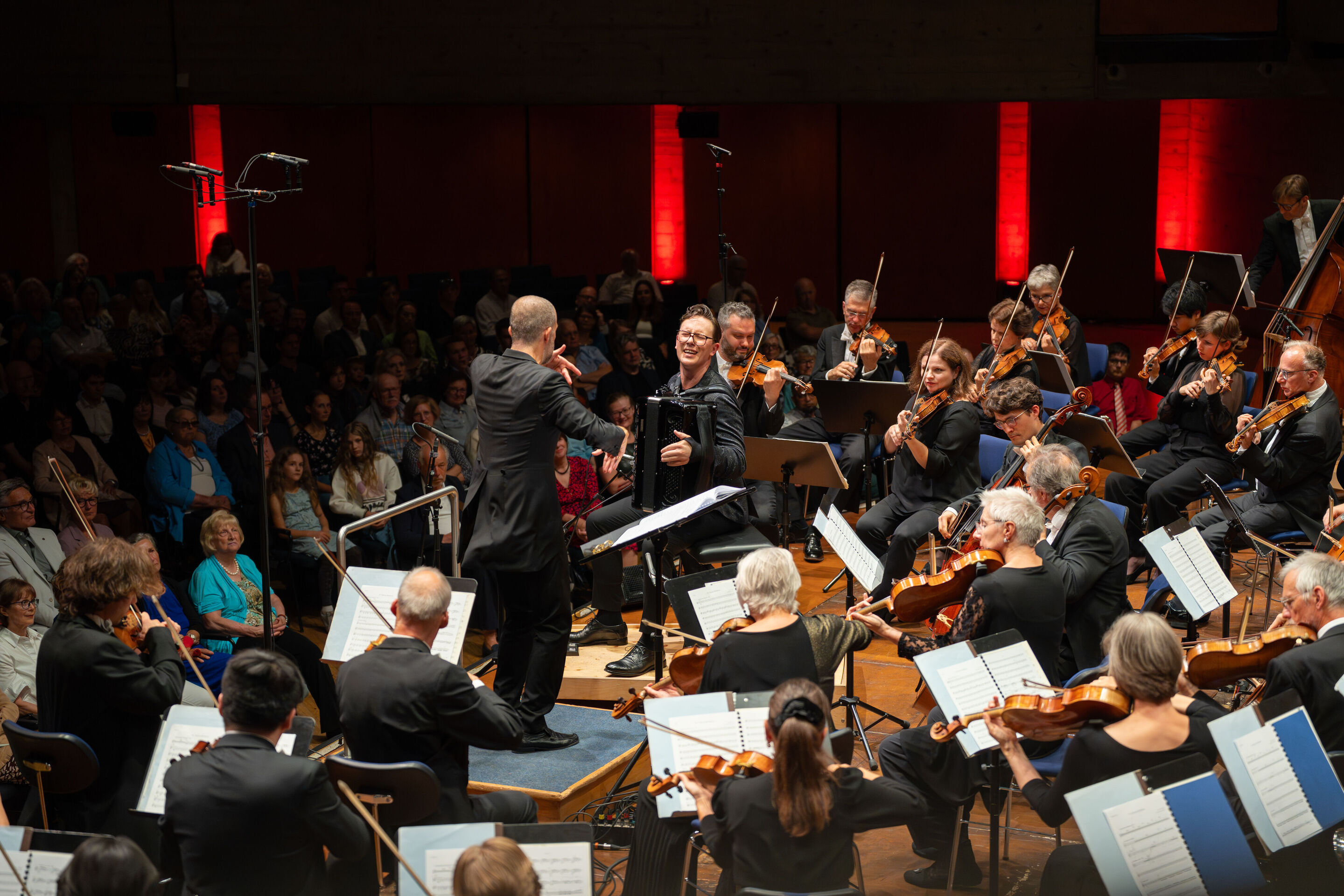 Abschlusskonzert mit Akkordeonstar Martynas Levickis und der Deutschen Kammerphilharmonie Bremen - Auf der Bühne des Festsaals Ingolstadt spielt Martynas Levickis auf seinem Akkordeon, dirigiert von Omer Meir Wellber links im Bild. Um sie herum spielen...