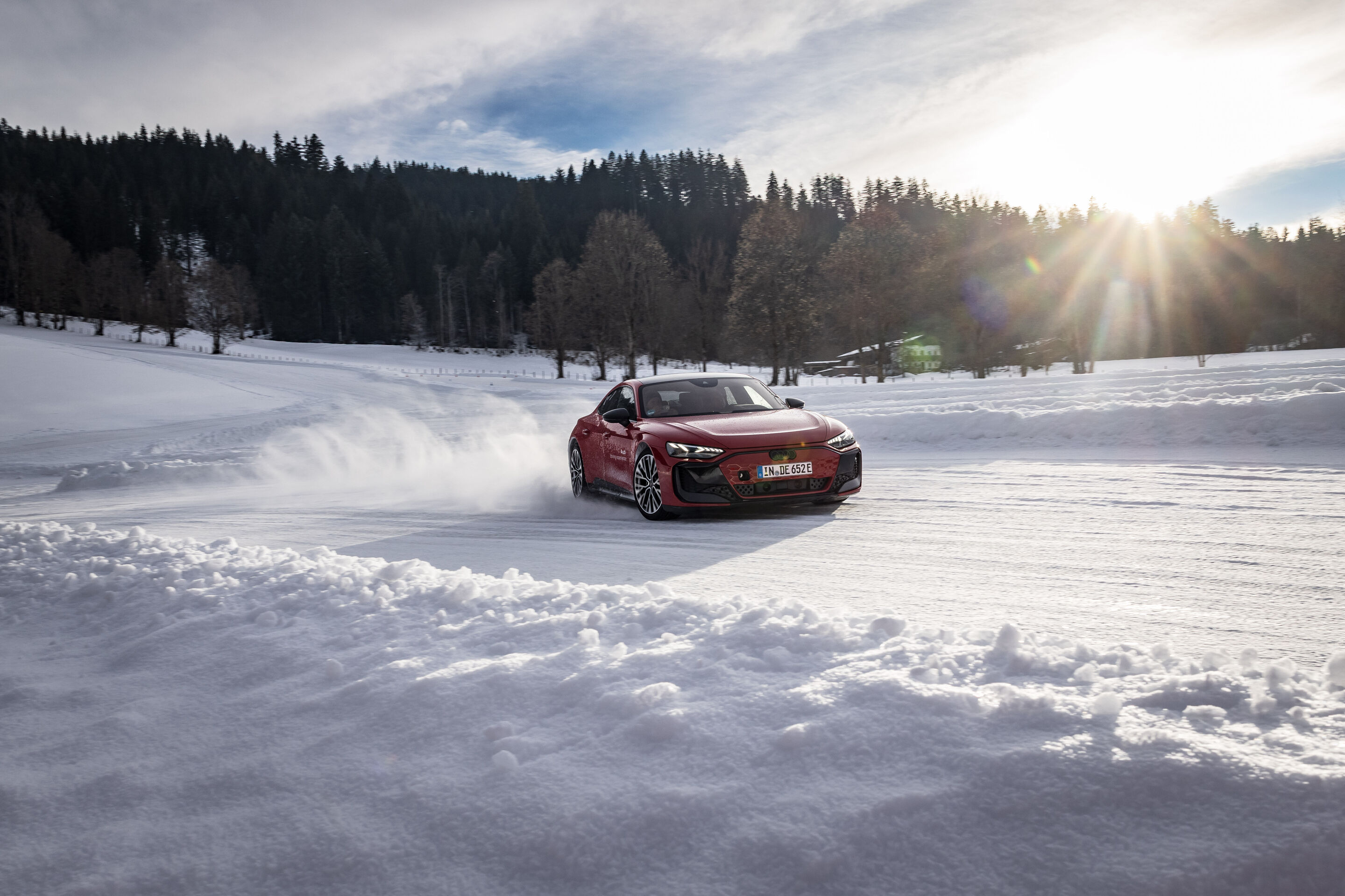 Audi RS e-tron GT - Der Audi RS e-tron GT fährt dynamisch über eine schneebedeckte Strecke und wirbelt dabei Schnee auf, im Hintergrund ein Wald unter der tief stehenden Sonne.
Farbe: Progressivrot Metallic, Outdoor Fahraufnahme, Exterieur, Dreiviertelfrontansicht
