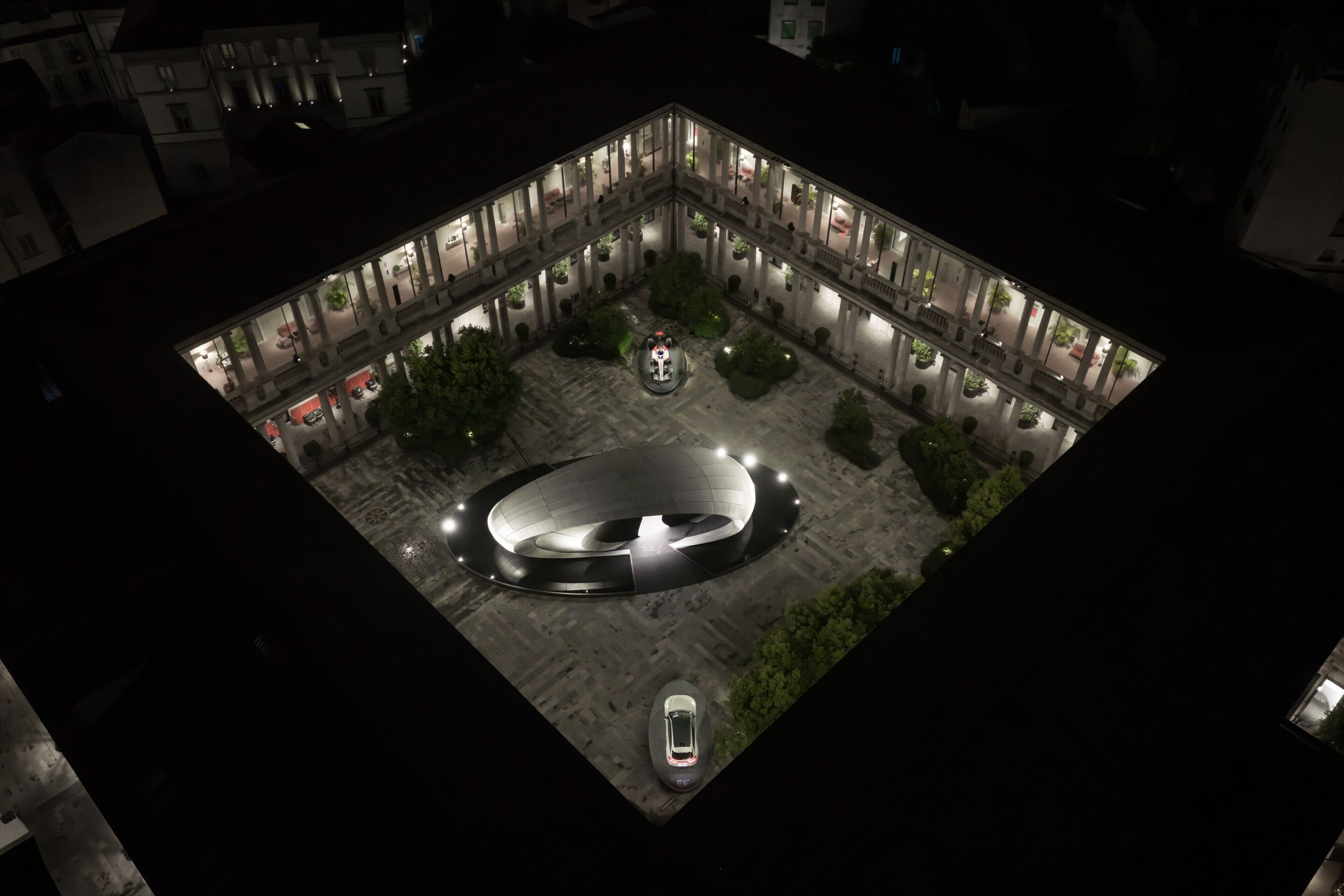 Audi auf der Milan Design Week 2026 - Nächtliche Luftaufnahme der Installation „Origin“ während der Milan Design Week 2026. Die reduzierte, ovale Form der architektonischen Struktur steht im Kontrast zur historischen Hofarchitektur und unterstreicht den...