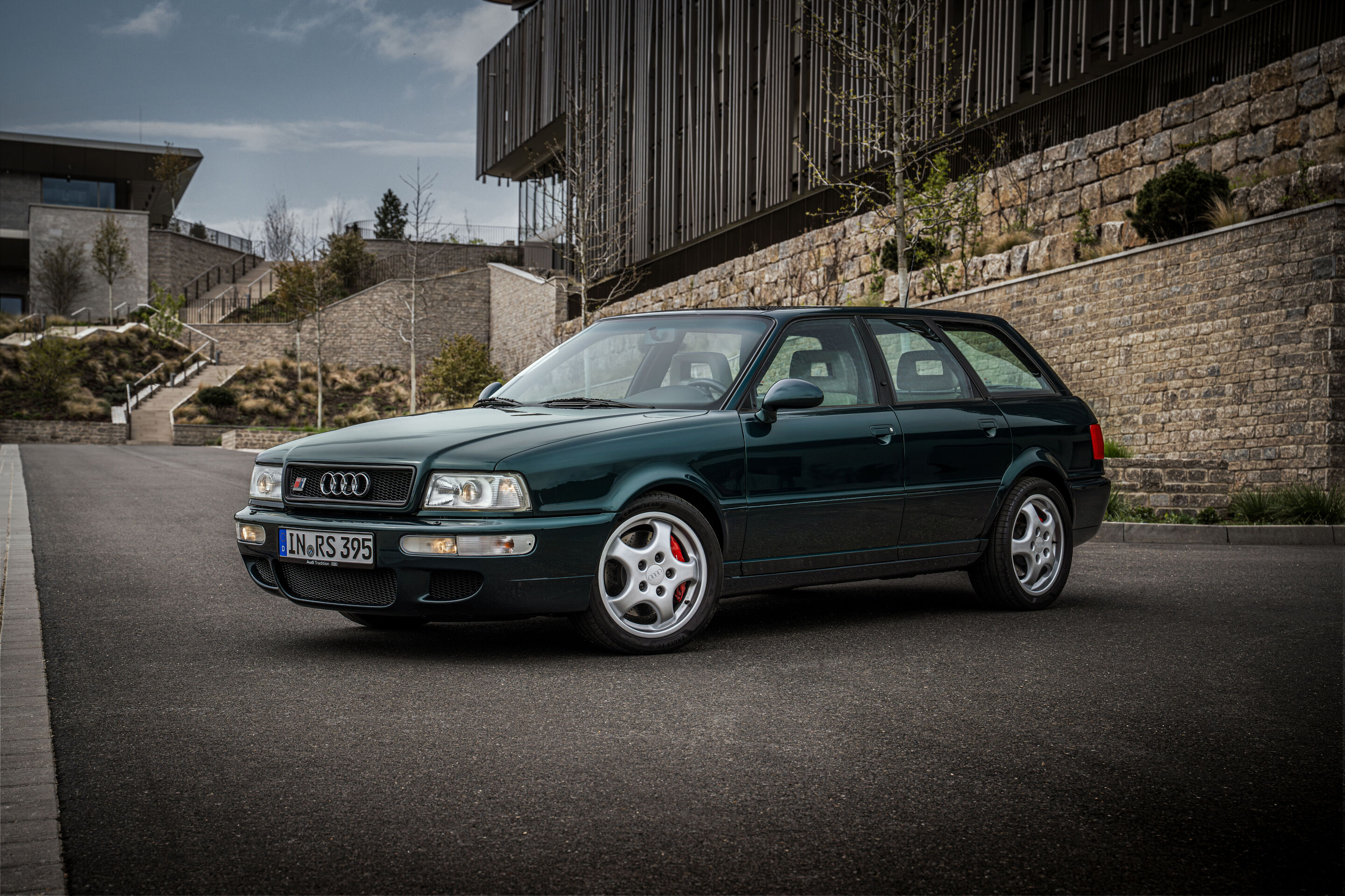 50 Jahre Fünfzylinder - Ein Audi RS2 Avant aus dem Jahr 1995 in dunkelgrüner Lackierung steht in Dreiviertel-Frontansicht auf einer geschwungenen Zufahrt vor einer Natursteinmauer.