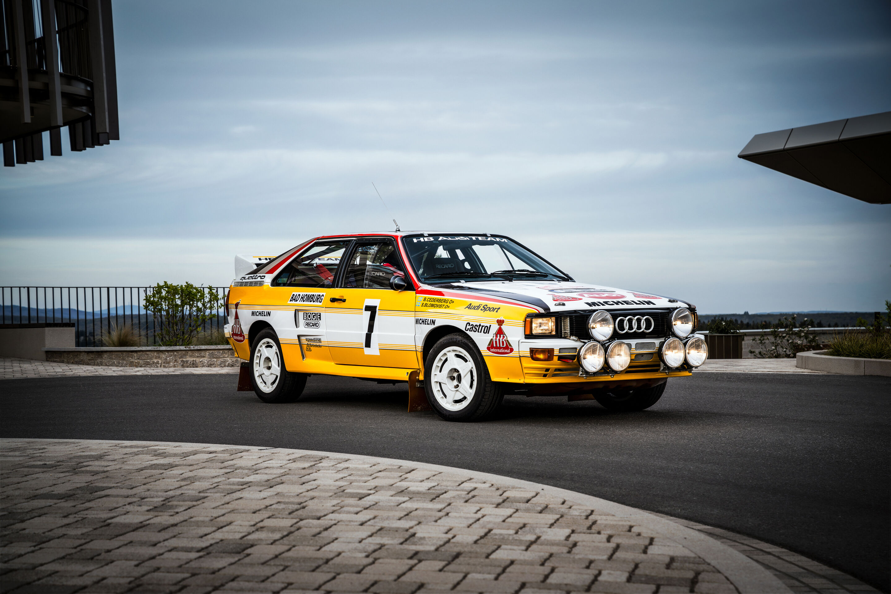 50 Jahre Fünfzylinder - Ein Audi Rallye quattro A2 von 1984 mit gelb-weißer Lackierung und Zusatzscheinwerfern steht auf einer Vorfläche.