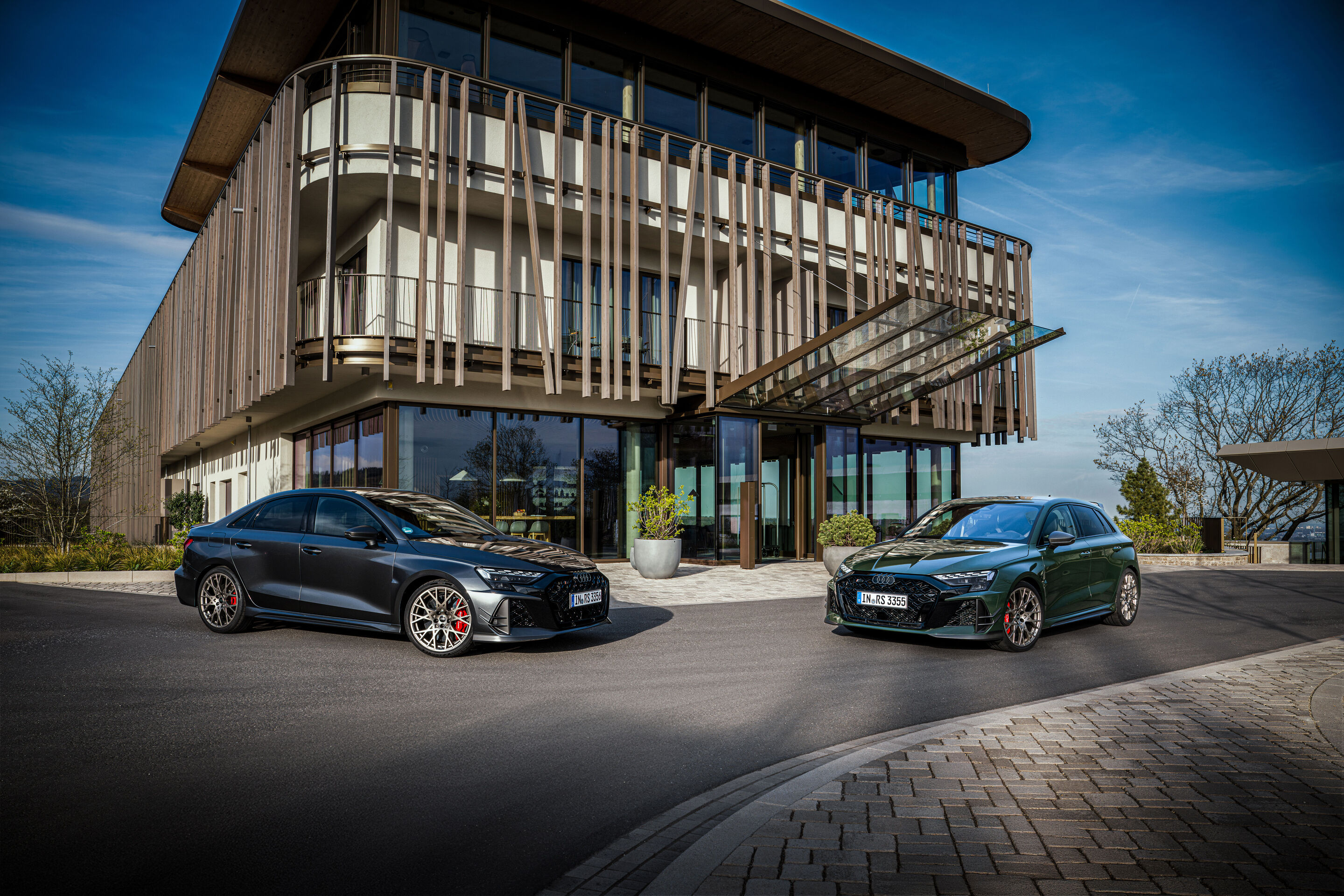 50 Jahre Fünfzylinder - Zwei Audi RS3 competition limited in Malachitgrün und Daytonagrau Perleffekt stehen frontal ausgerichtet vor einem zeitgenössischen Gebäude.
