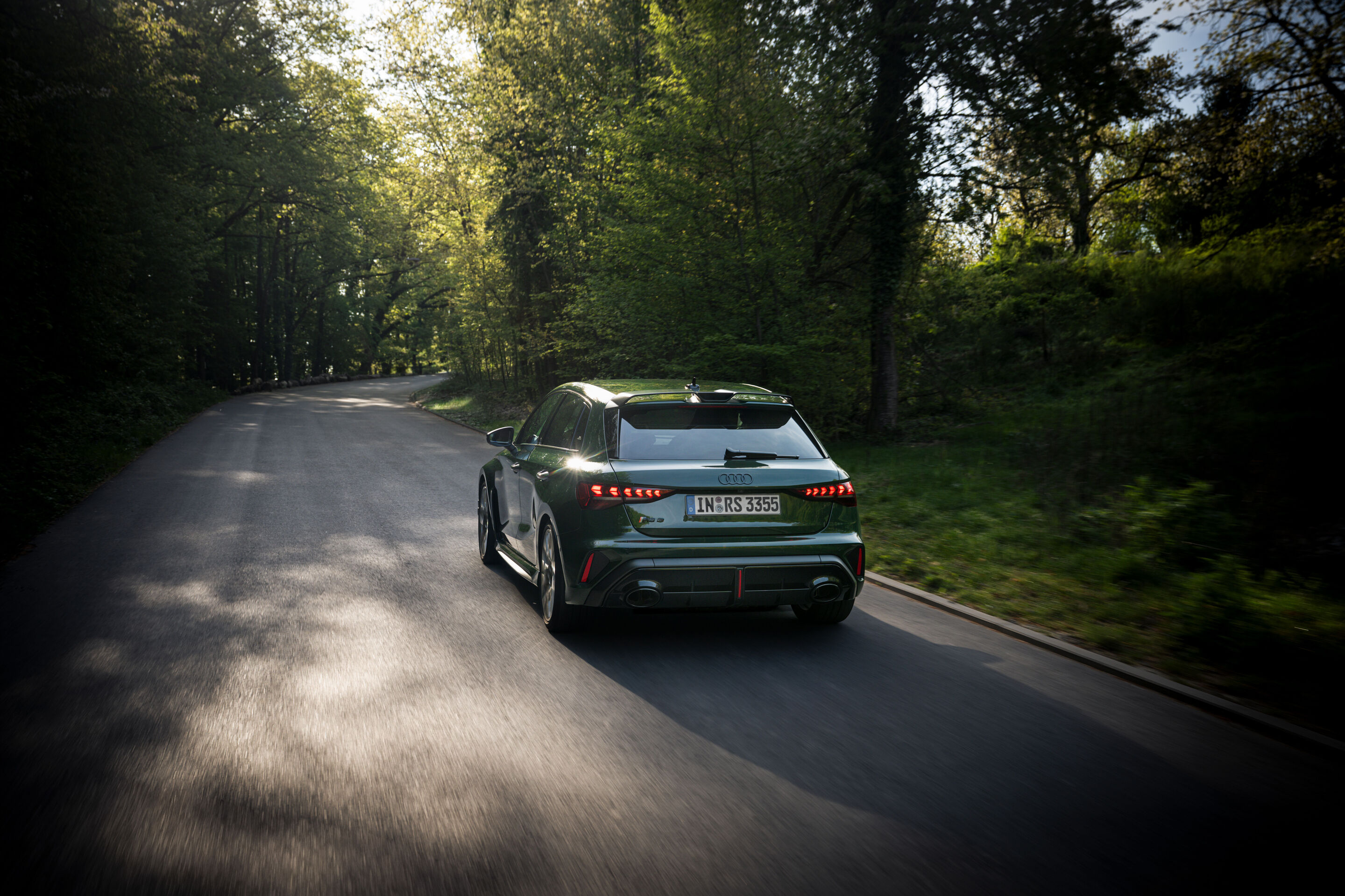 50 Jahre Fünfzylinder - Ein Audi RS3 competition limited (malachitgrün) fährt auf einer schmalen Straße durch ein bewaldetes Gebiet, aufgenommen aus der Heckperspektive mit Bewegungsunschärfe.