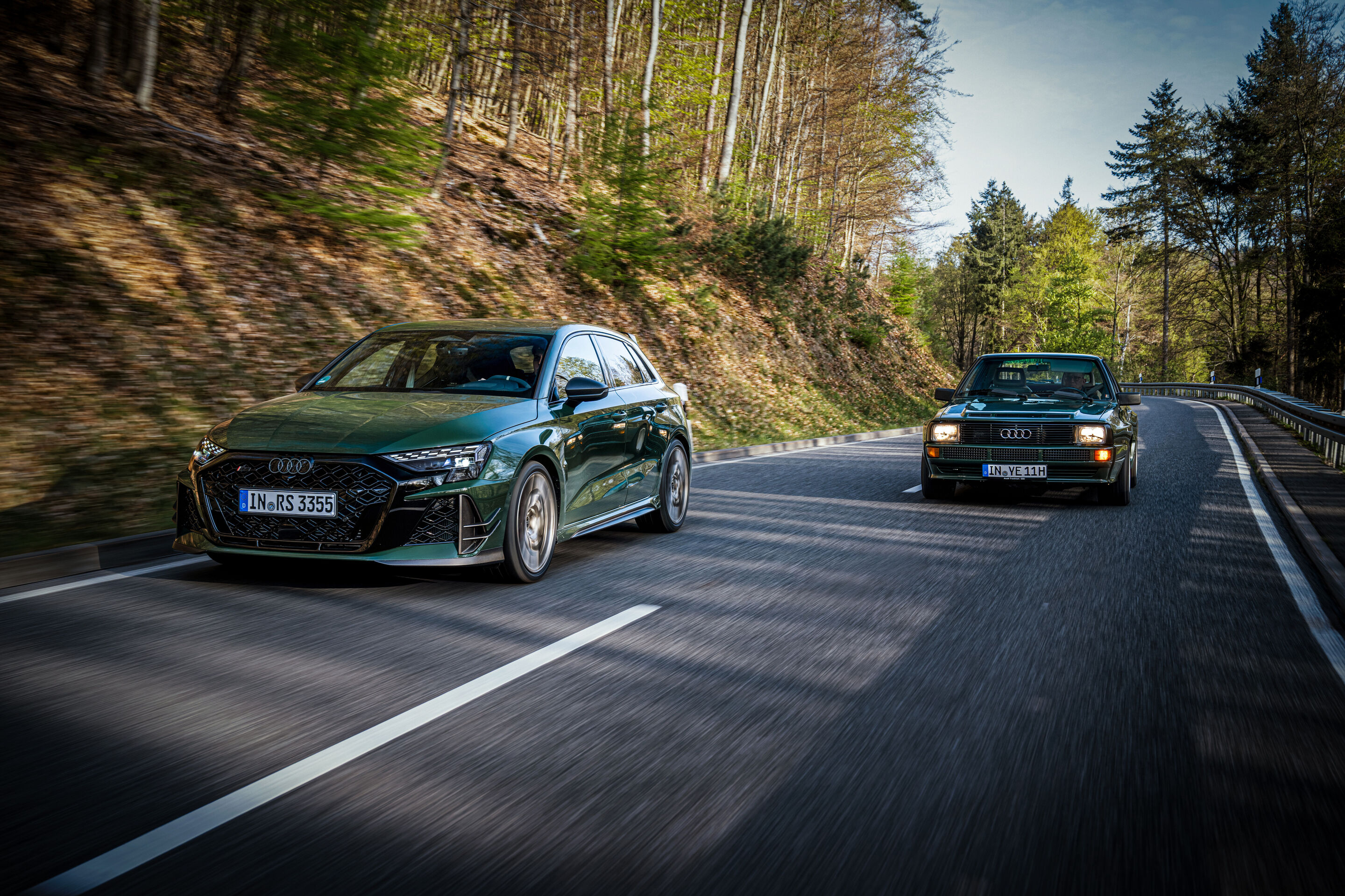 50 Jahre Fünfzylinder - Ein Audi RS3 competition limited fährt vor einem historischen Audi Sport quattro auf einer kurvenreichen Straße durch den Wald.