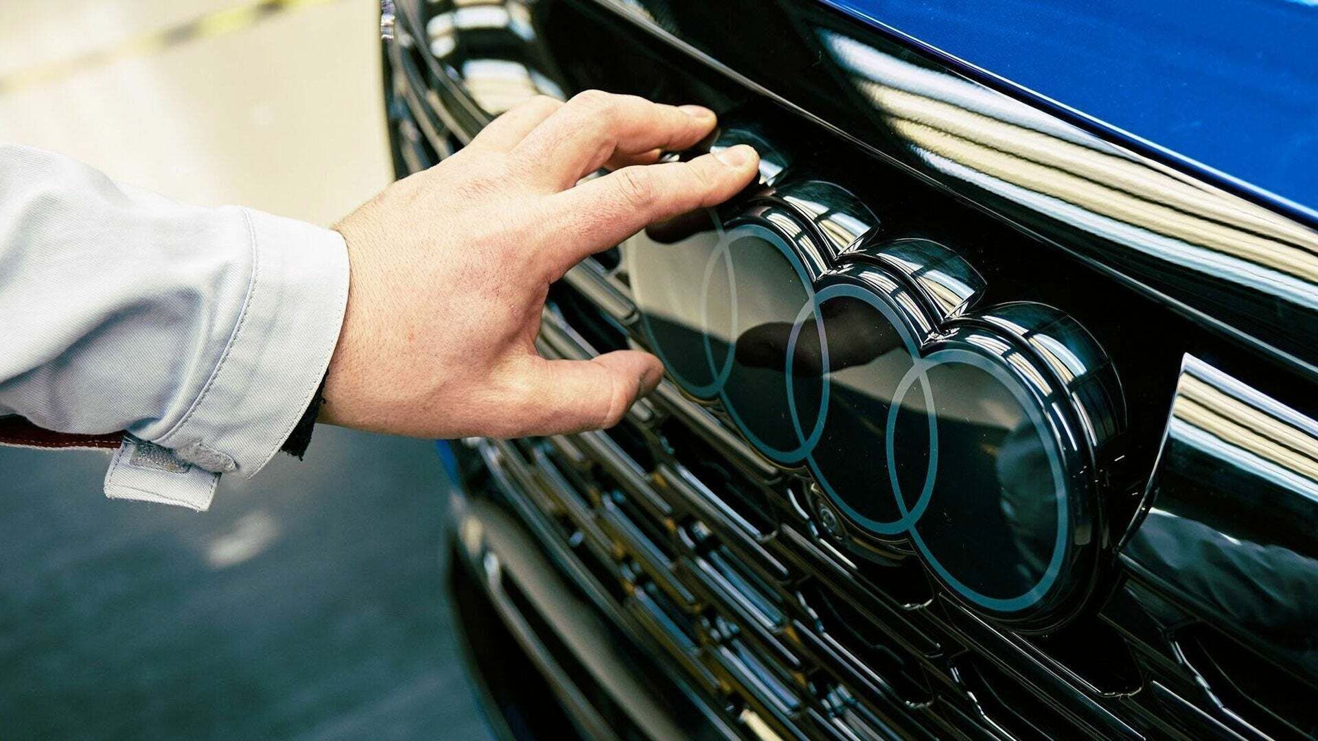 A hand touches the Audi logo on the front of a vehicle - A hand touches the Audi logo on the front of a vehicle