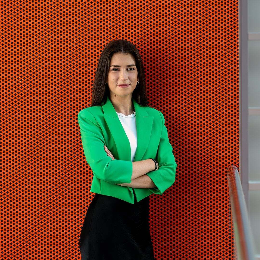 Alina stands with her arms crossed in front of a wall and smiles at the camera