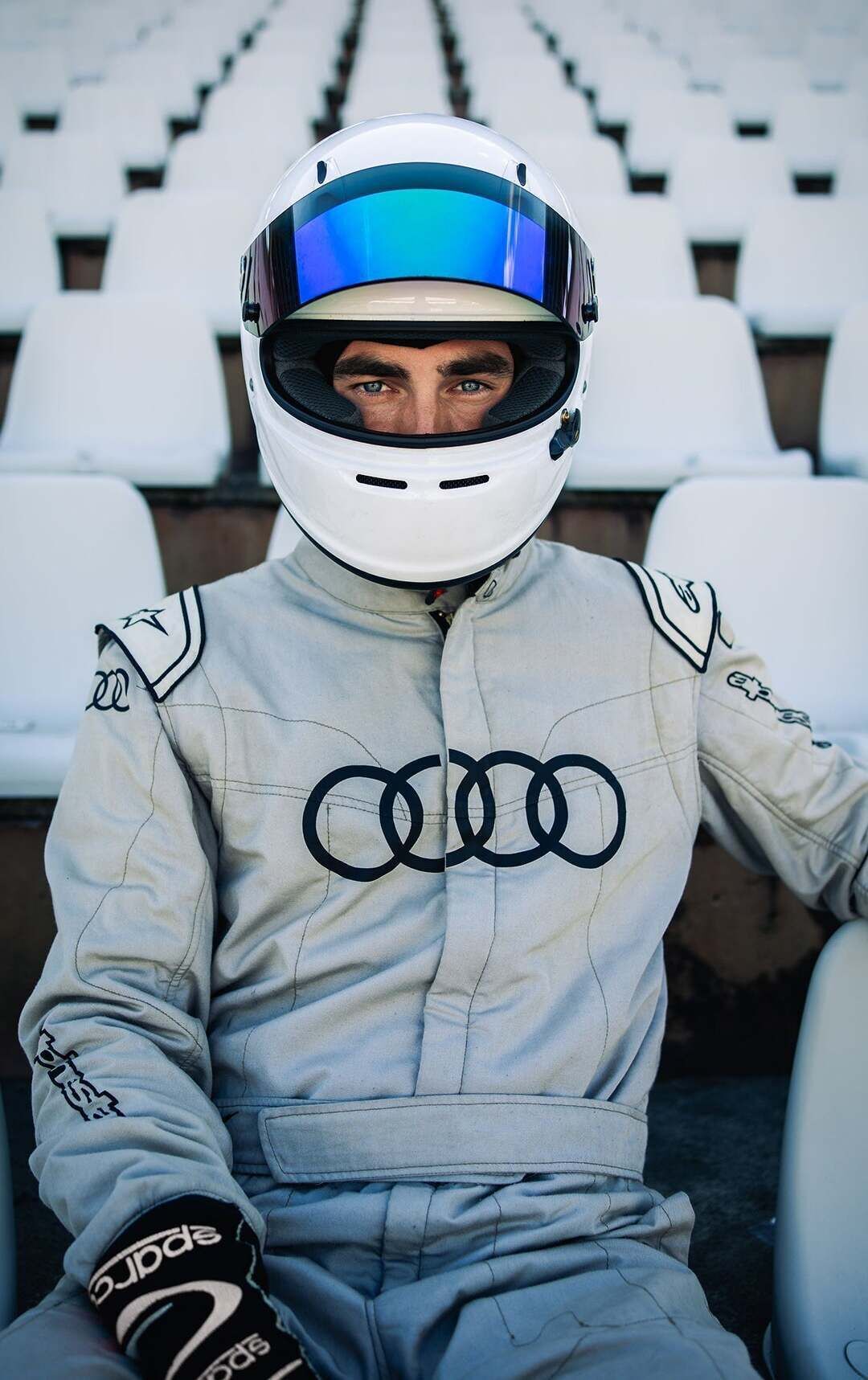 Formula Student - The TUfast racing driver is wearing a helmet, sitting on an empty grandstand and facing the camera