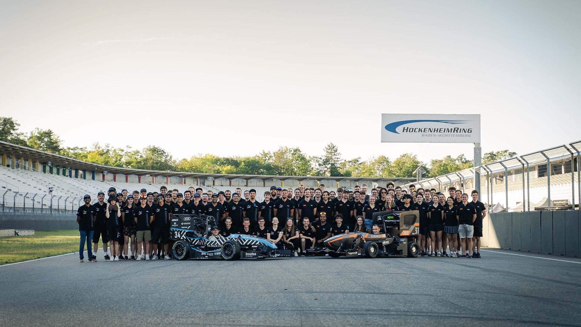 Group photo of the TUfast e.V. and Schanzer Racing e.V. teams with their vehicles at the Hockenheimring