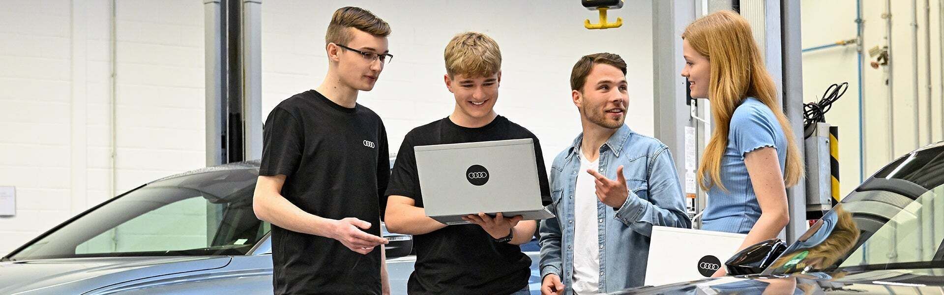 Four Audi employees are talking and looking at something on a laptop