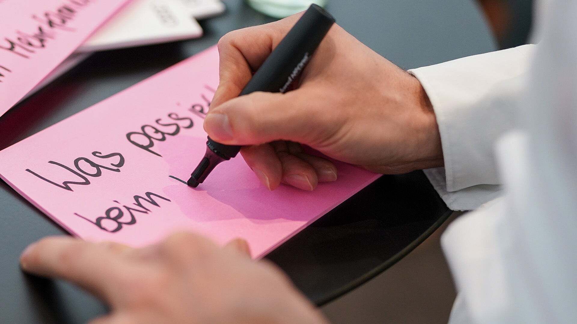 A close-up of a hand writing something on pink paper