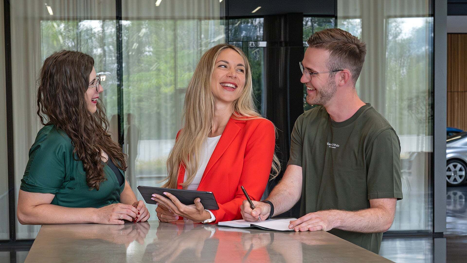 Three people are smiling to each other and one is holding an IPad