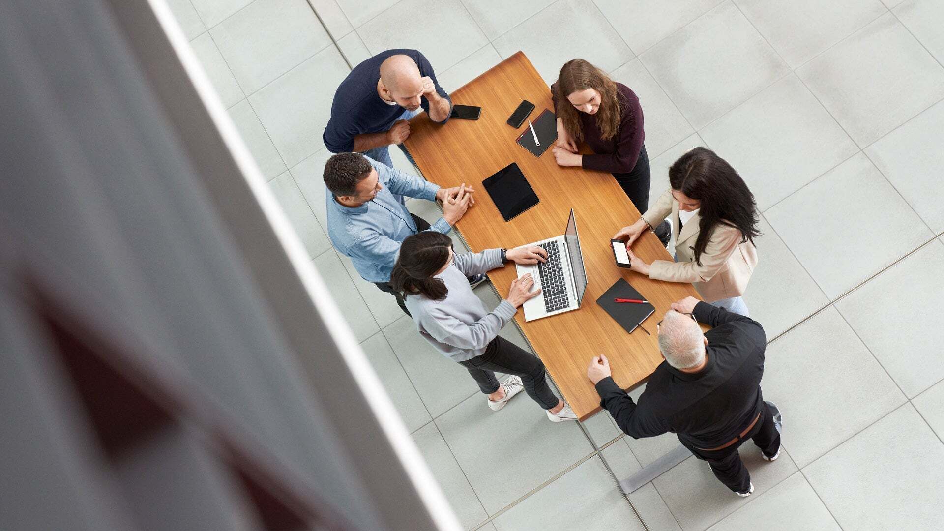 Aus der Vogelperspektive betrachtet: Sechs Personen stehen um einen Tisch mit Laptops und diskutieren gemeinsam.