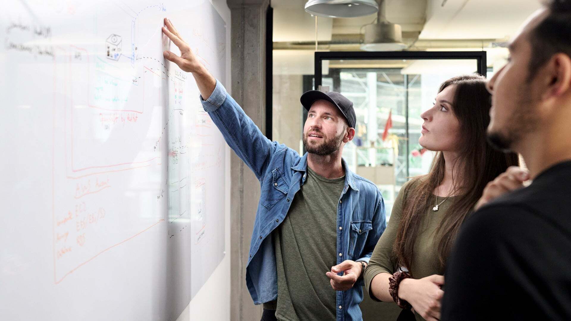Drei Personen stehen an einem Whiteboard, betrachten Notizen und diskutieren gemeinsam.