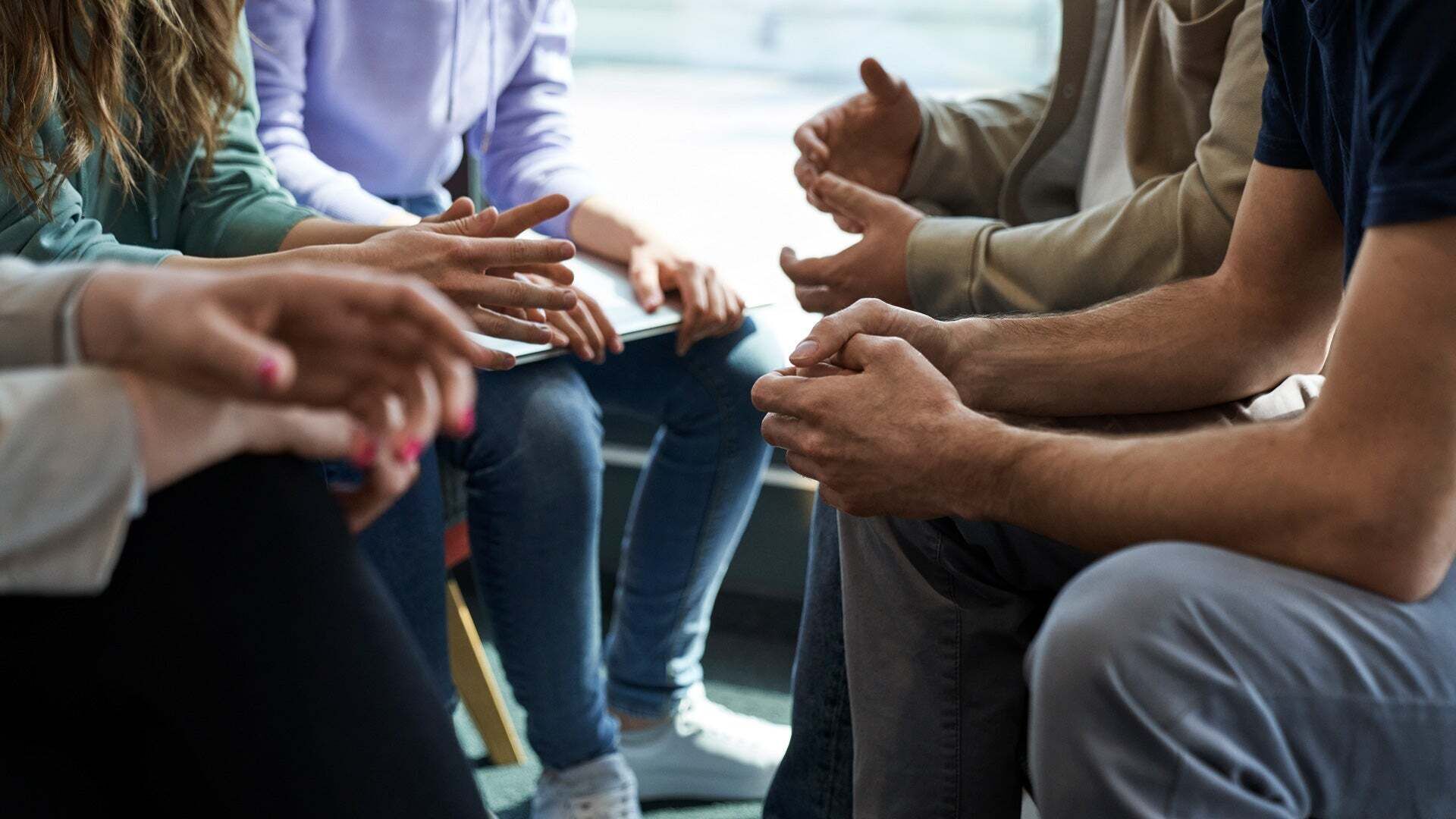 Mehrere Personen sitzen im Kreis und gestikulieren während eines Gesprächs, der Fokus liegt auf ihren Händen.