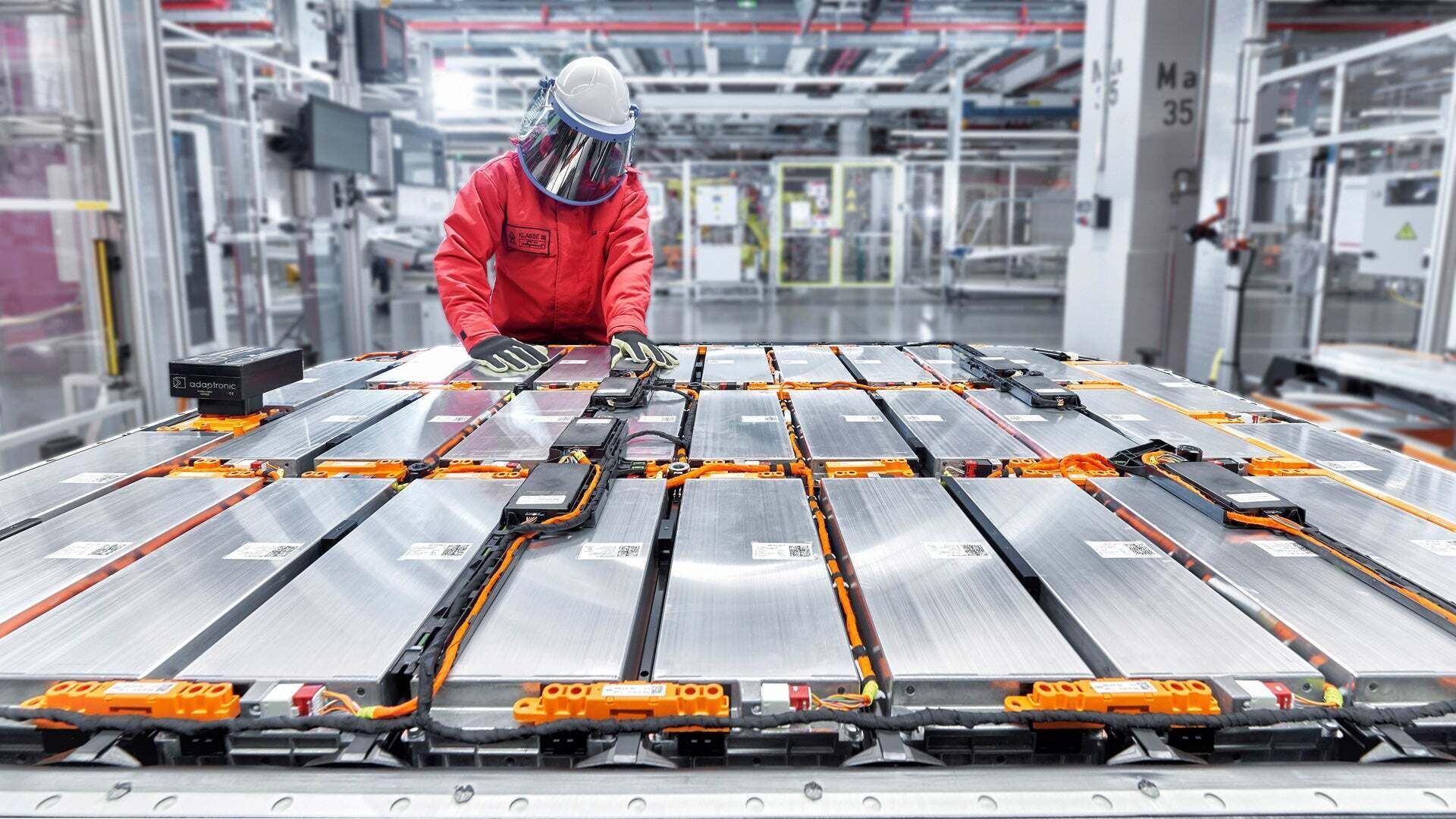 Eine Person in Schutzkleidung arbeitet in einer Produktionshalle an einem großen Batteriemodul.