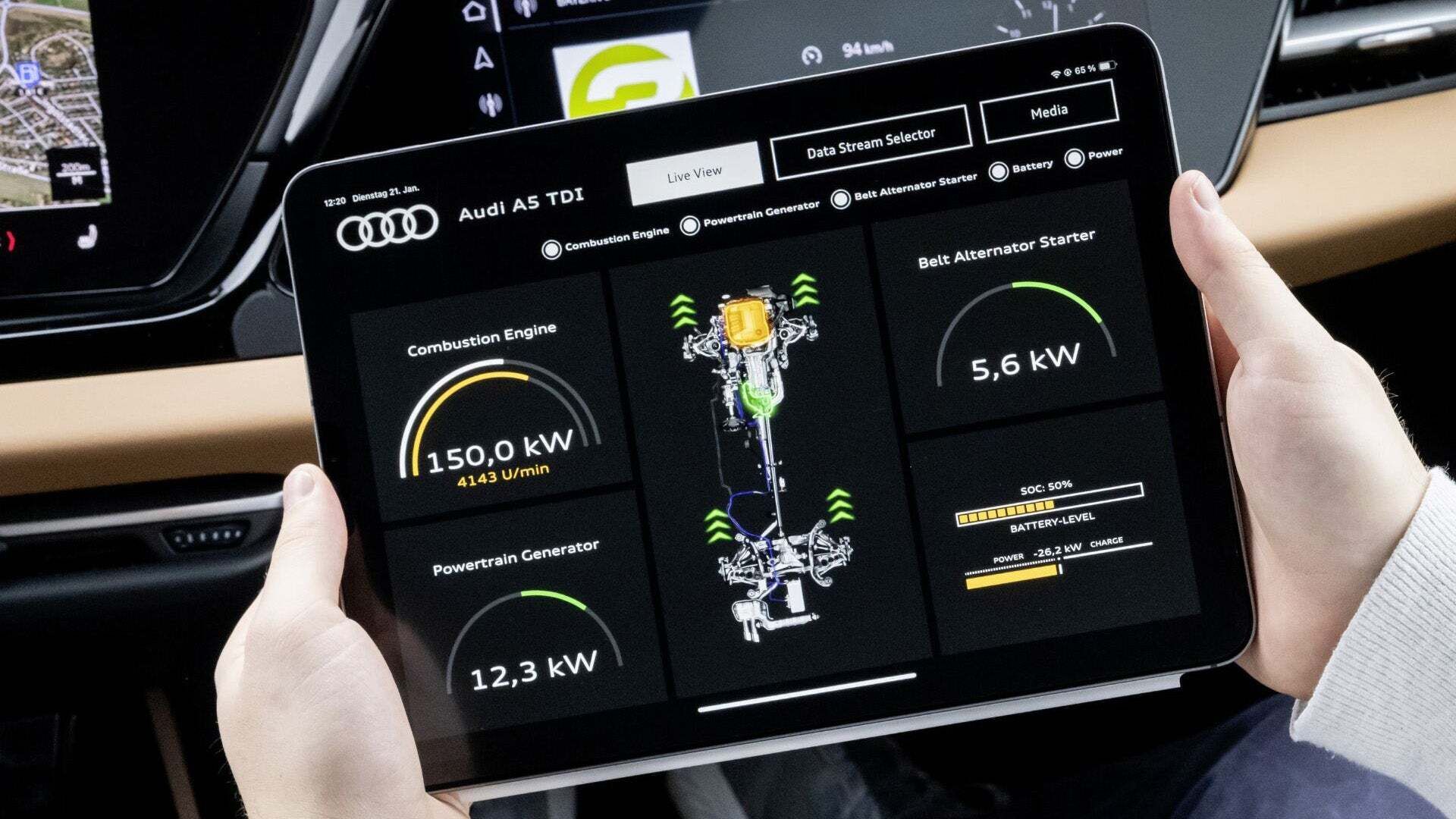 Ein Fahrer hält ein Tablet in einem Audi A5 TDI. Auf dem Bildschirm wird eine Echtzeit-Diagnose des Fahrzeugs angezeigt, inklusive Daten zu Verbrennungsmotor, Generator und Batterie. Im Hintergrund ist das Armaturenbrett mit einem digitalen Display und Navigationssystem zu sehen.