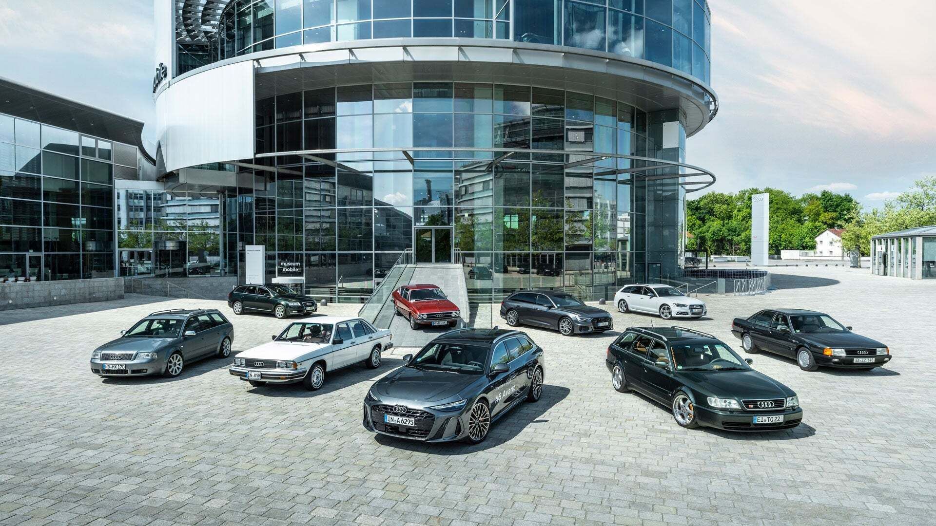 Audi C-series models are lined up in a star shape in front of the round glass façade of the Audi museum mobile.