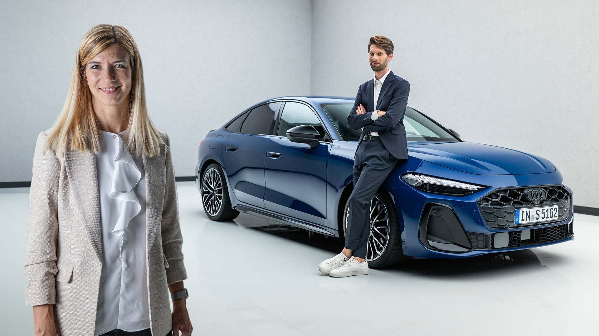Luisa Werther steht im Vordergrund, im Hintergrund lehnt Jakob Hirzel an einem blau lackierten Audi A5 - Audi S5 Limousine TFSI: Kraftstoffverbrauch kombiniert in l/100 km: 7,8-7,4; CO₂-Emissionen kombiniert in g/km: 178-169; CO₂-Klasse: F