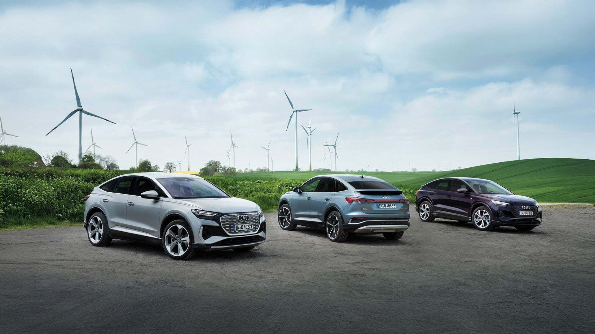 Mehrere Audi Q4 Sportback e-tron Modelle vor einer Wiese mit Windrädern