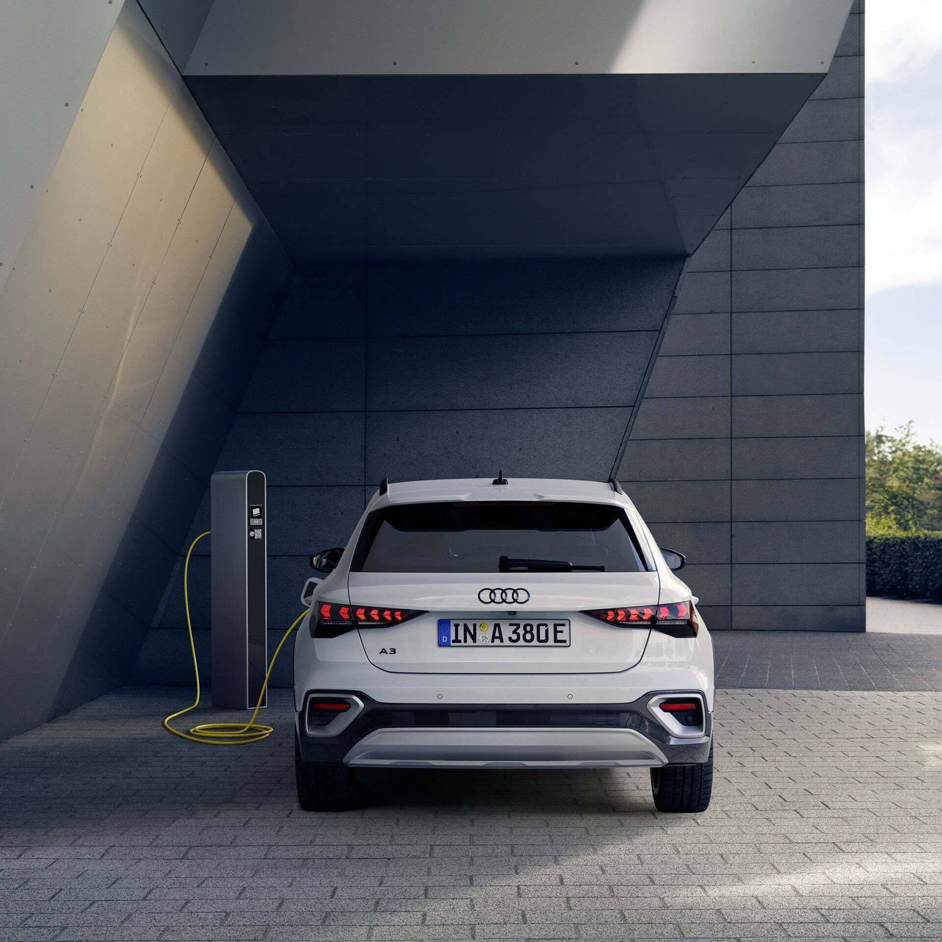 The back of a white Audi A3 allstreet TFSI e at the charging station in front of a modern concrete façade