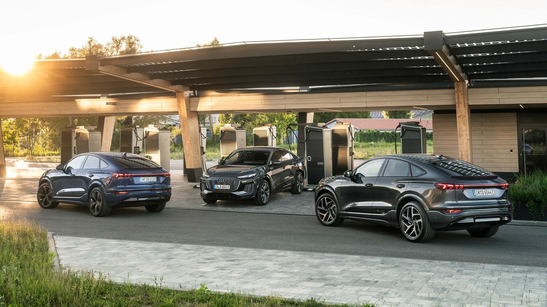 Three Audi Q6 Sportback e-tron cars at an Audi charging hub. One is charging while the others drive to the charging stations under the beige roof structure.